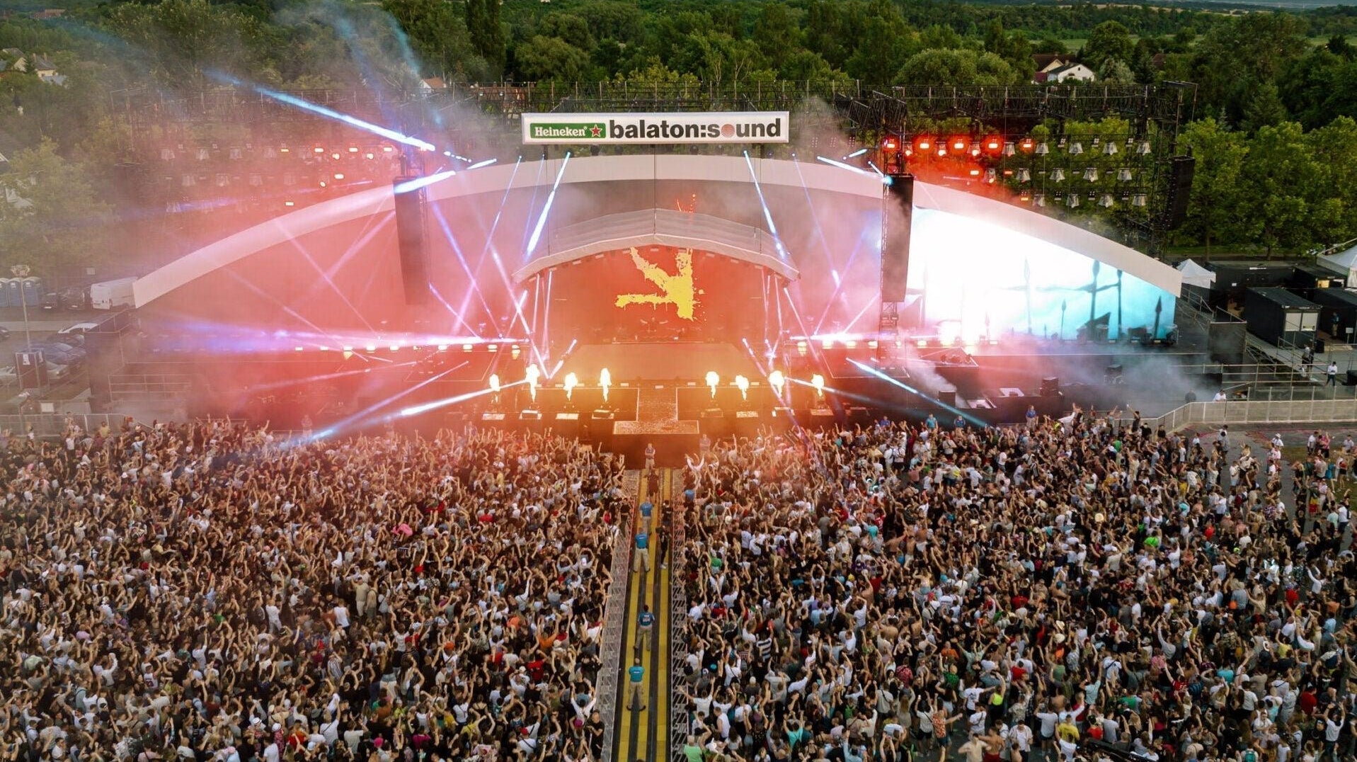 Aerial view of a massive crowd at Balaton Sound's brightly lit main stage with laser lights.