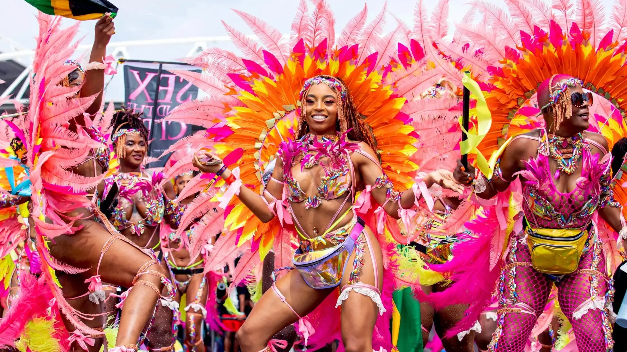 Carnival performers in vibrant pink and orange feathered costumes with intricate beadwork, celebrating Caribana.