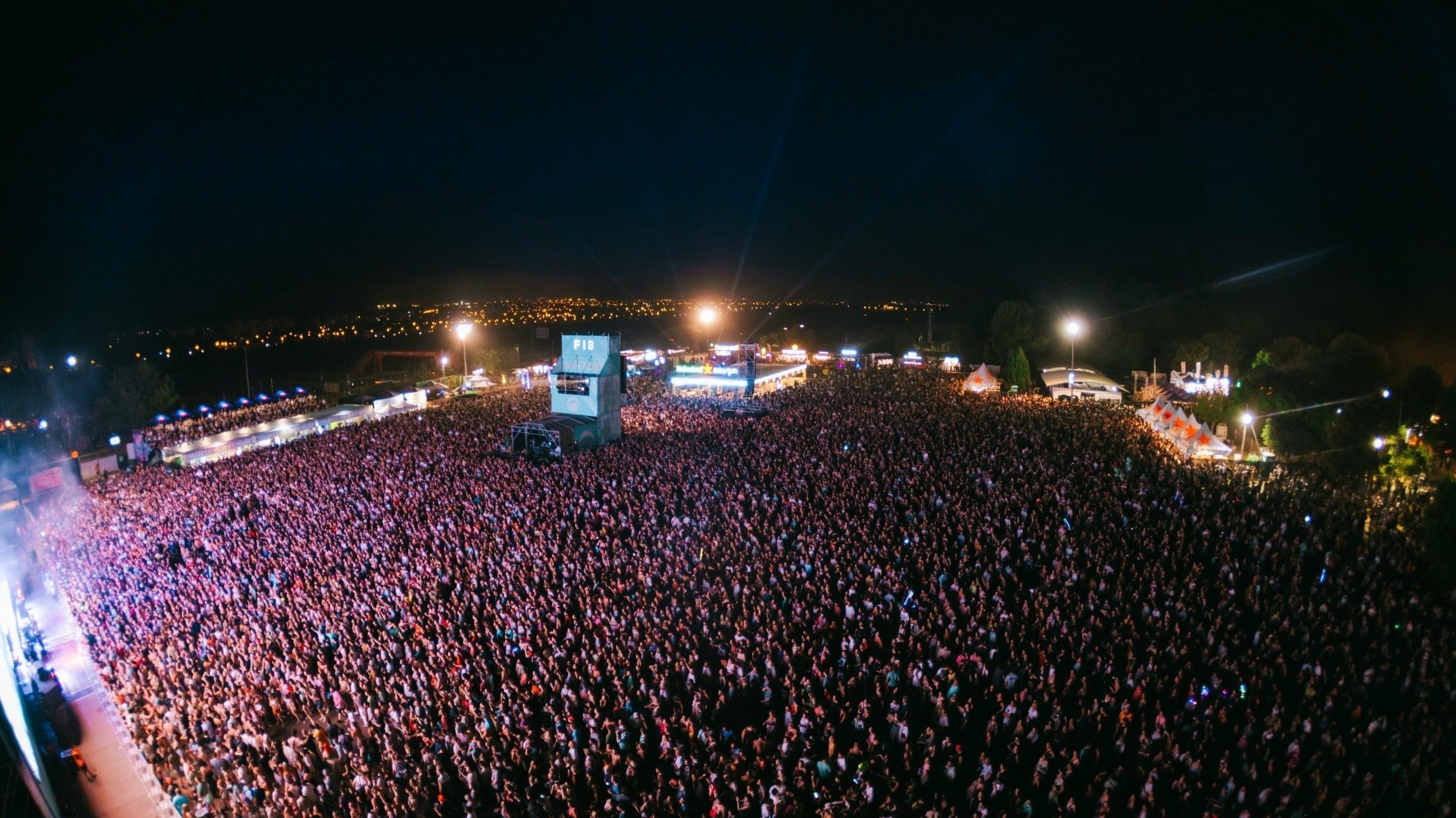 Vast crowd at FIB Benicassim festival at night, stage lights illuminating the audience under a dark sky.