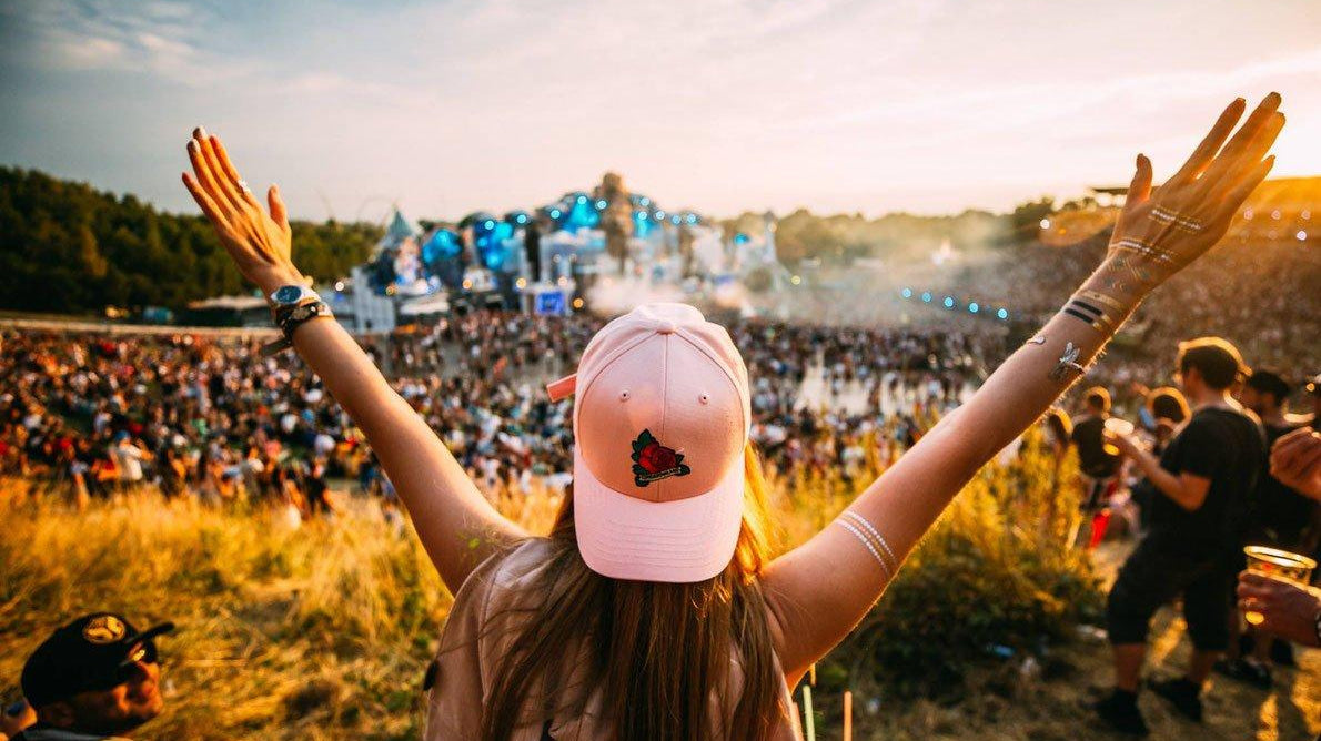 Person in a pink cap with arms raised, enjoying a vibrant outdoor music festival at sunset.