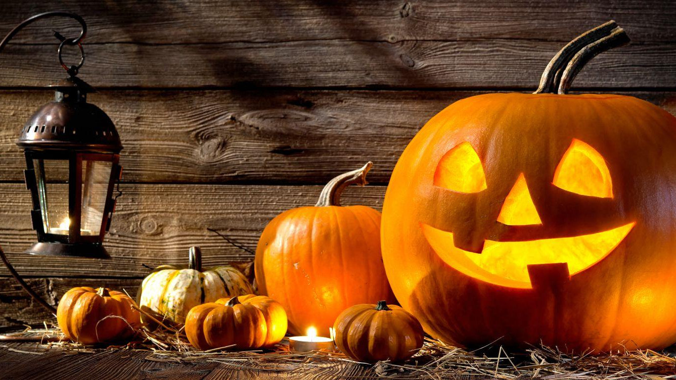 Glowing jack-o'-lantern, small pumpkins, and a lit lantern against rustic wood for Halloween.