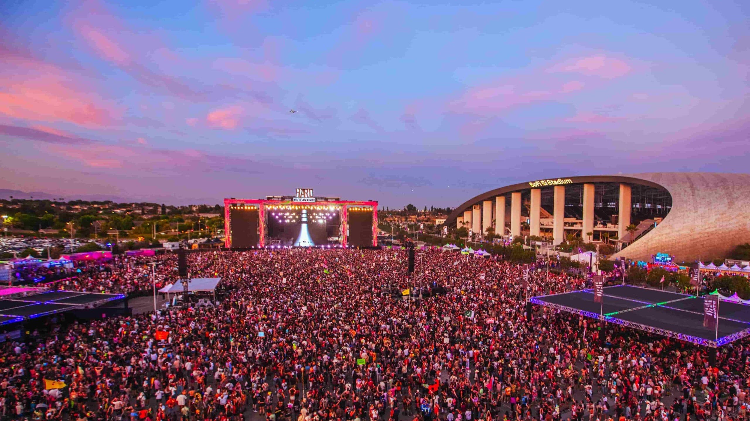 HARD Summer electronic music festival crowd at sunset, with a large stage and SoFi Stadium in the background.