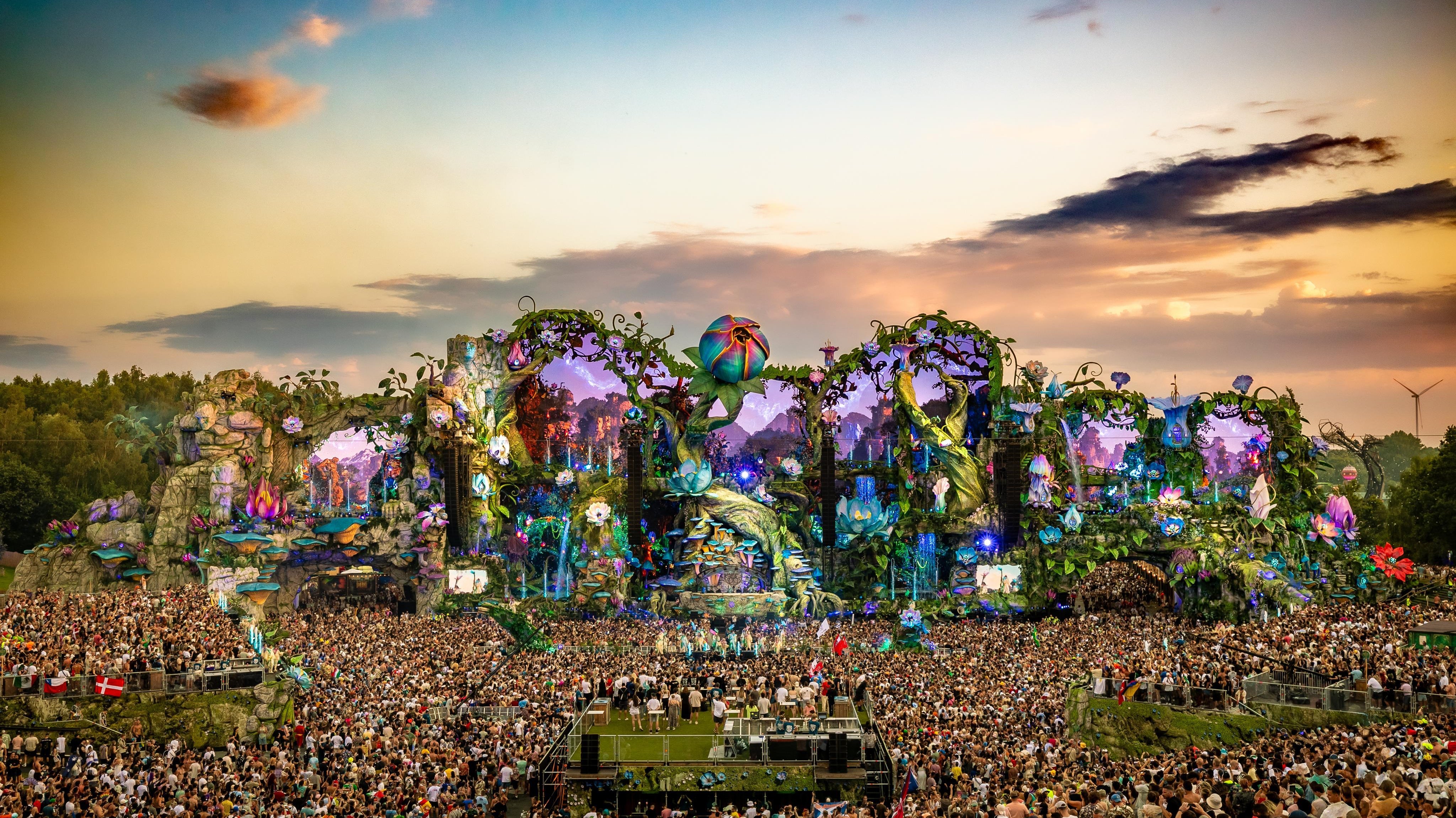 Tomorrowland main stage at sunset, with a massive crowd and intricate, fantastical decorations.