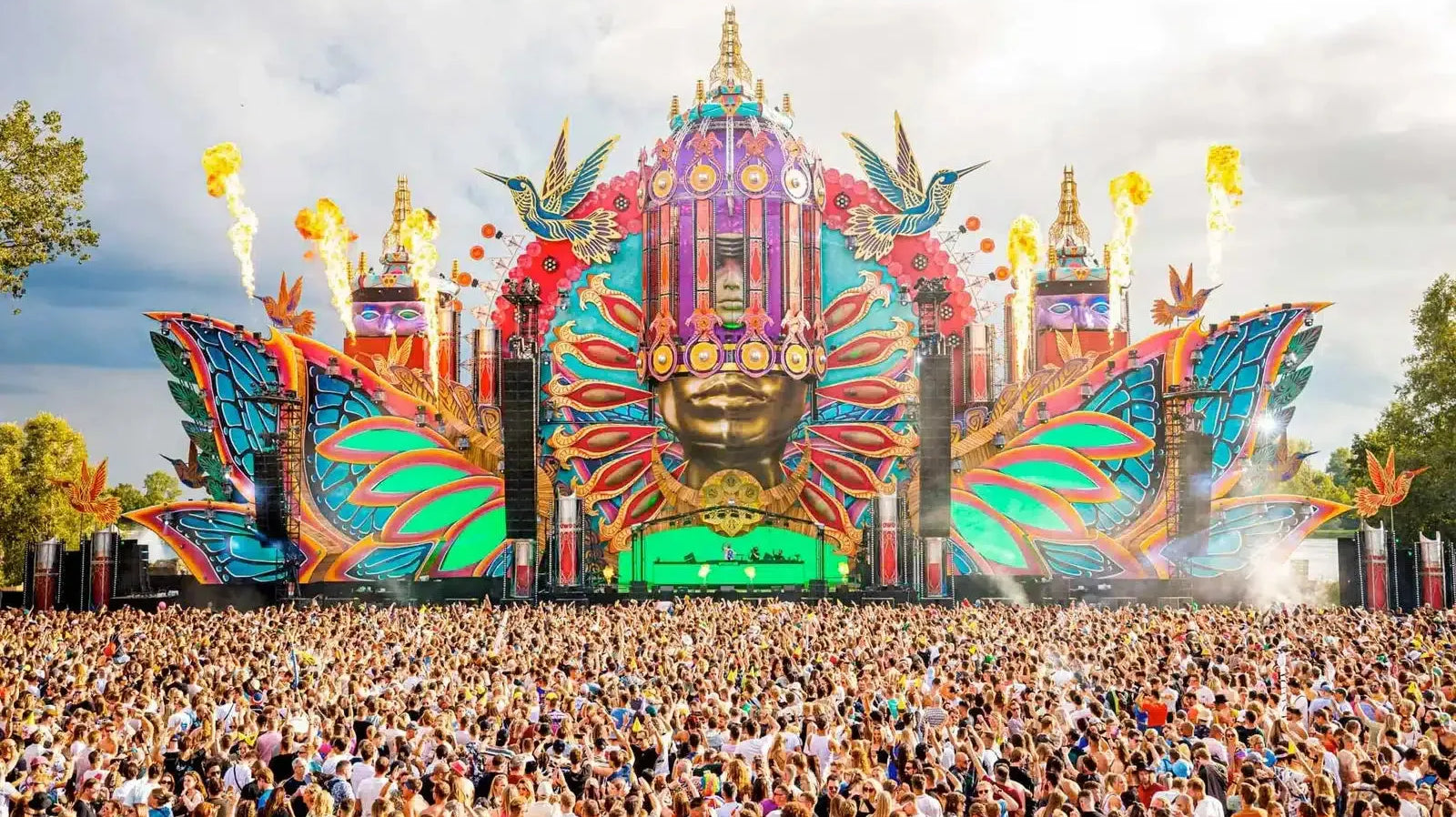Vibrant Mysteryland main stage with a large golden face, colorful wings, and pyrotechnics over a massive crowd.