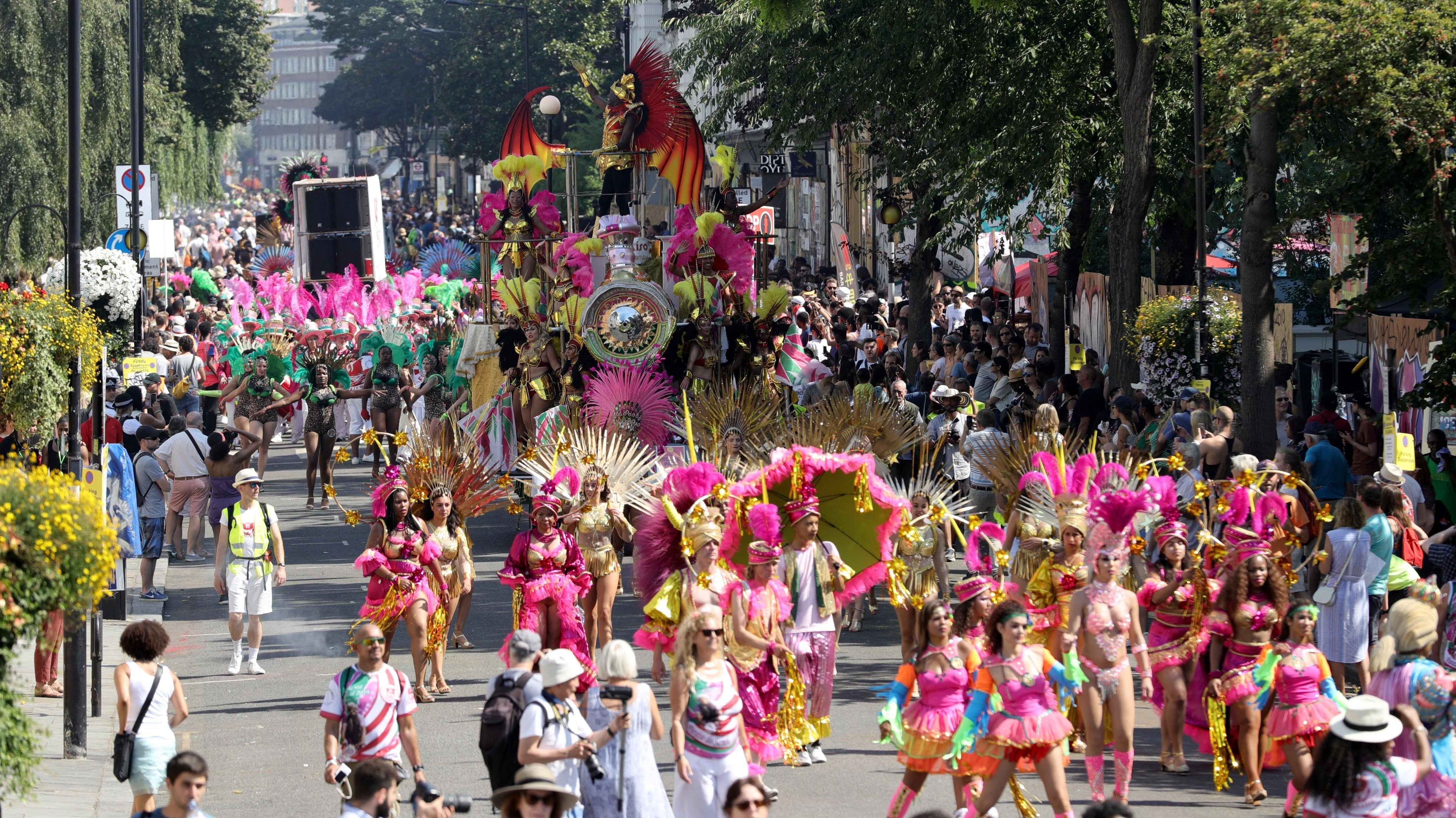 Vibrant Notting Hill Carnival parade with dancers in elaborate pink and gold costumes and a large float.