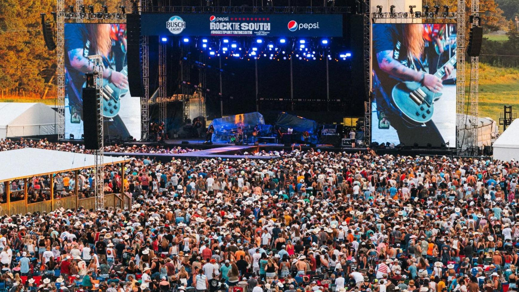 Crowd of country music fans at Rock the South festival, with a large stage and video screens.