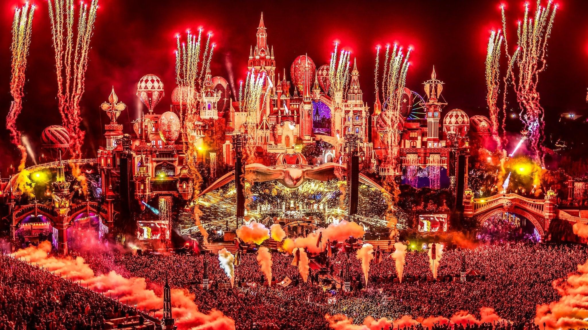 Tomorrowland mainstage at night, illuminated by red fireworks and lights over a massive crowd.