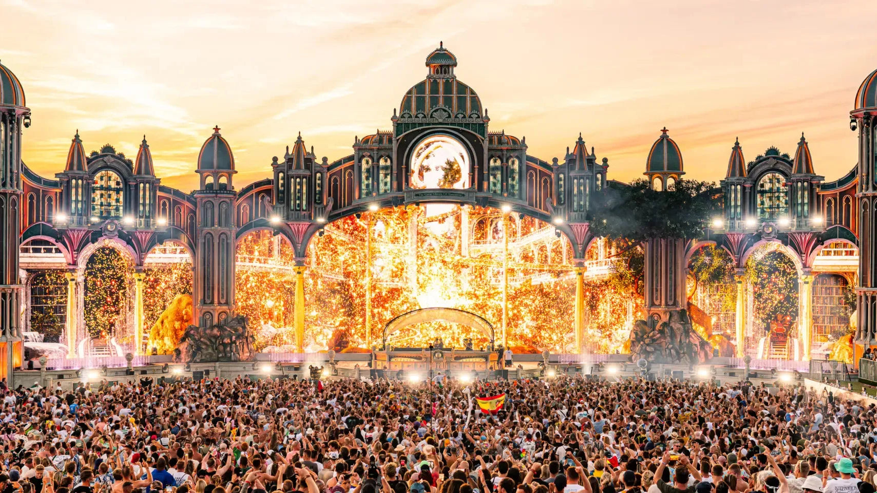 Tomorrowland's CONSCIENCIA main stage at sunset, with golden lights, fireworks, and a massive crowd.