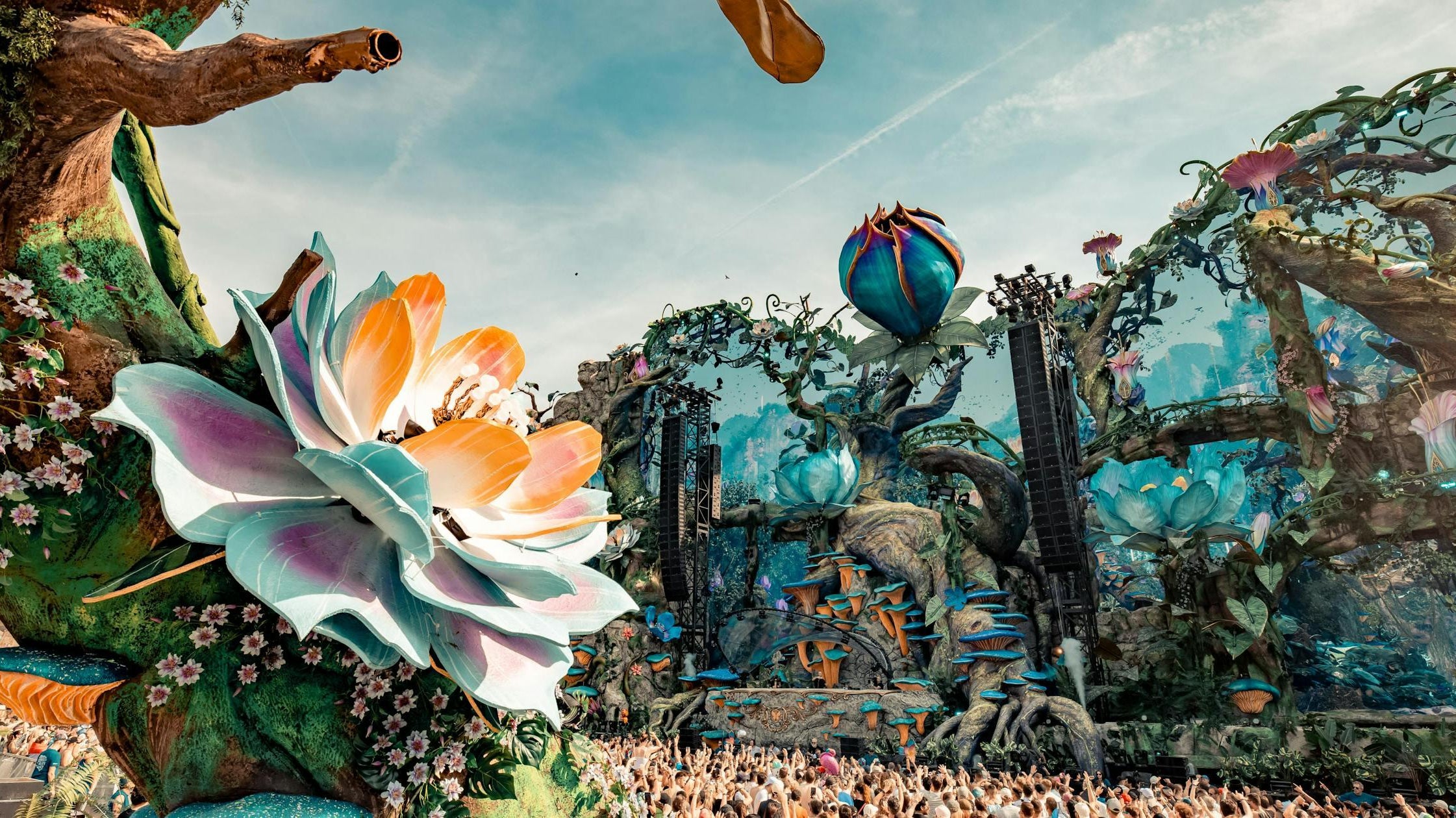 Tomorrowland Brasil main stage with vibrant floral decor, lush trees, and a huge crowd.