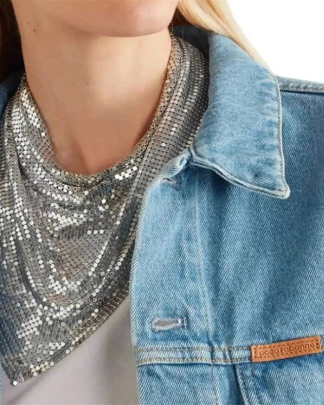 Silver liquid metal mesh scarf draped over a woman's neck, worn with a denim jacket.