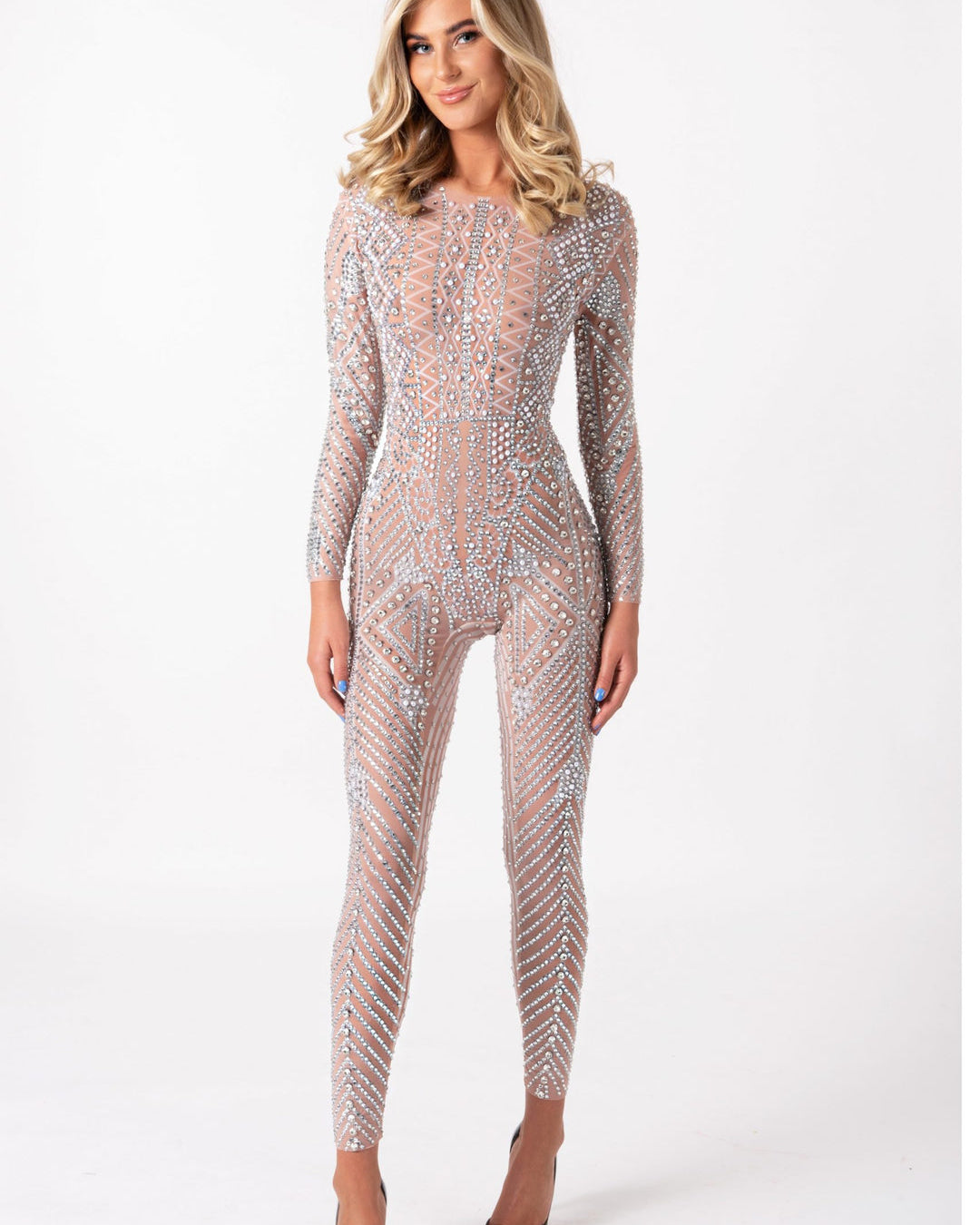 Model wearing a long-sleeve, nude-toned jumpsuit covered in intricate, hand-glued silver rhinestones in a geometric pattern.