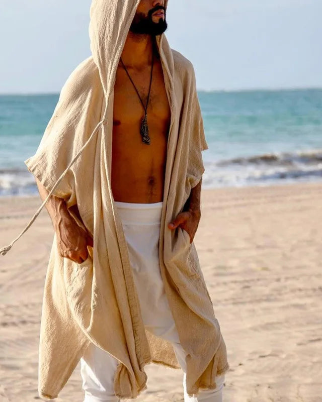 Men's sand polyester hooded cape with wide bat-wing sleeves and pockets, worn on a beach.
