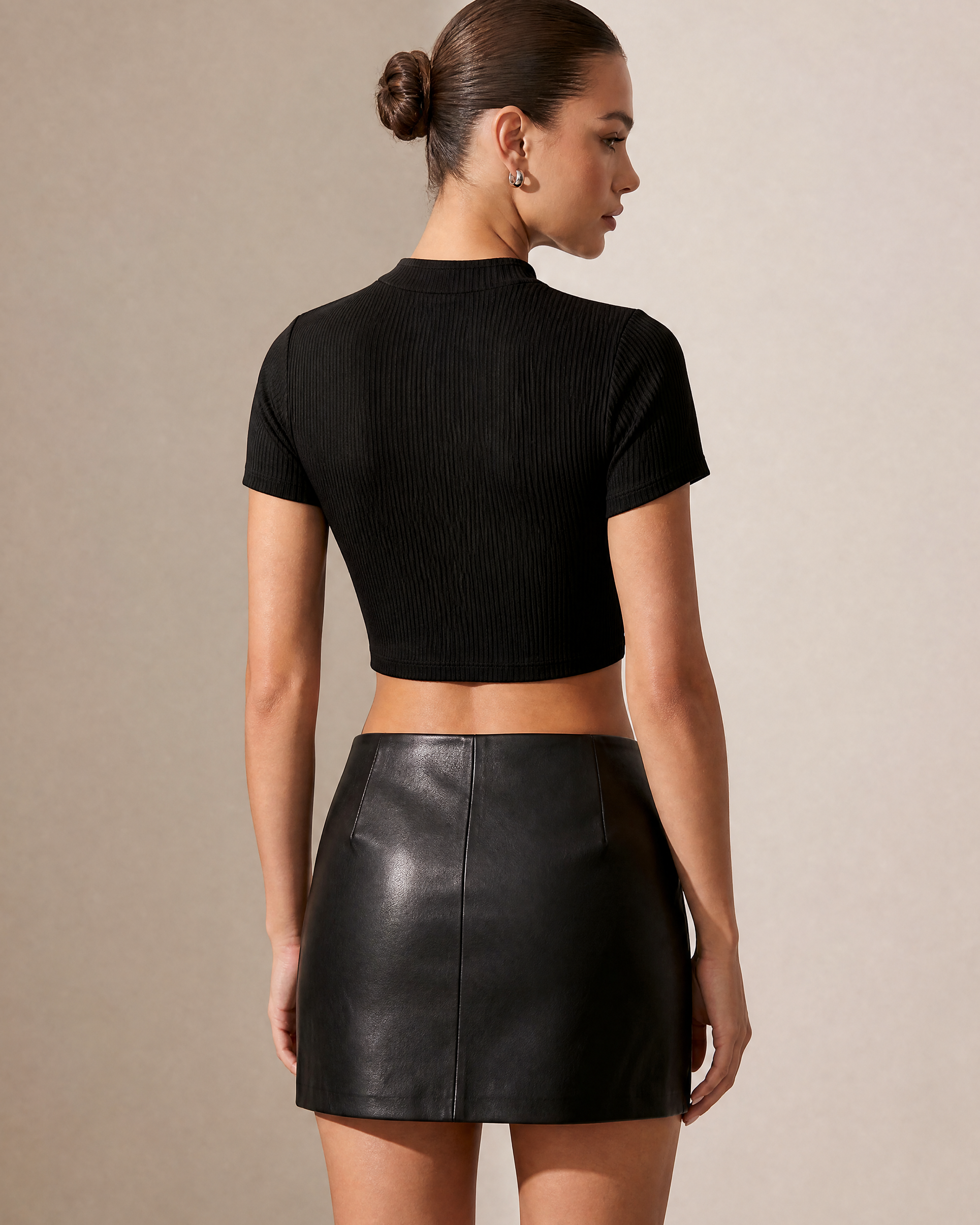 Model from behind wearing a black ribbed crop top and black leather mini skirt.