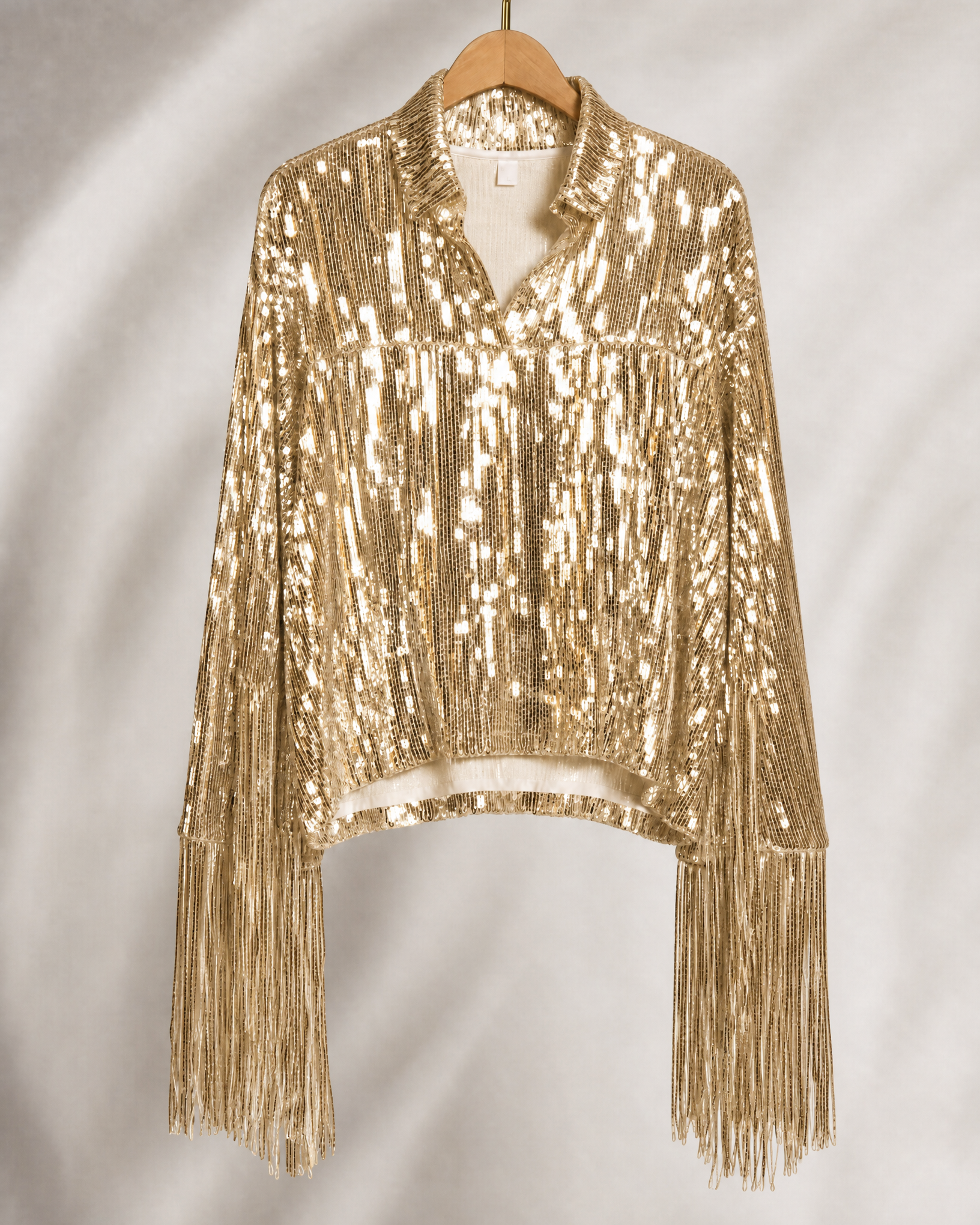 Gold sequin fringe jacket with long sleeves, hanging on a wooden hanger.
