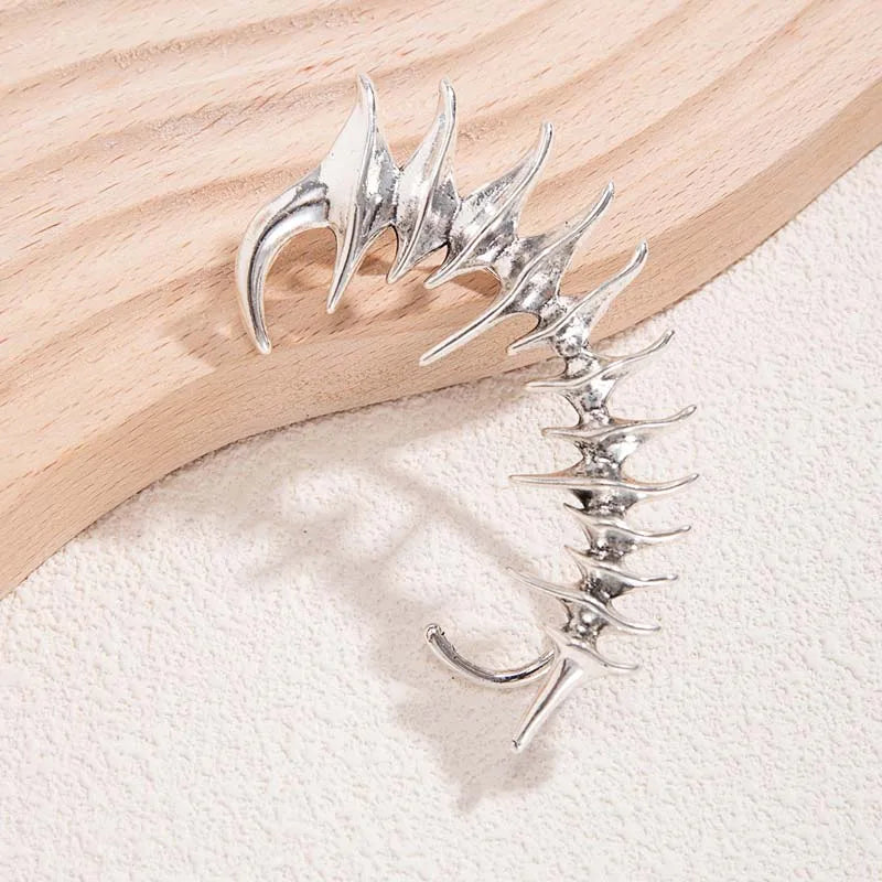 Ear Cuff Cyberpunk in metallo argento con punte angolari affilate in un design a colonna vertebrale biomeccanica, senza bisogno di piercing.