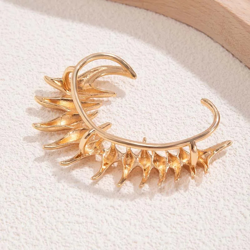 Ear cuff in metallo color oro con punte angolari affilate in un design a colonna vertebrale biomeccanica, avvolgente l'intero orecchio.