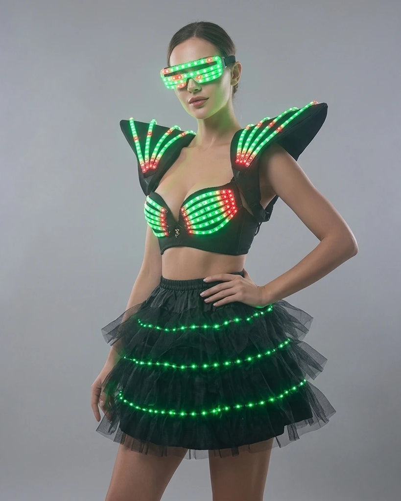 Model wearing a futuristic black LED tutu bra set with glowing green and red lights, shoulder pieces, and matching visor.