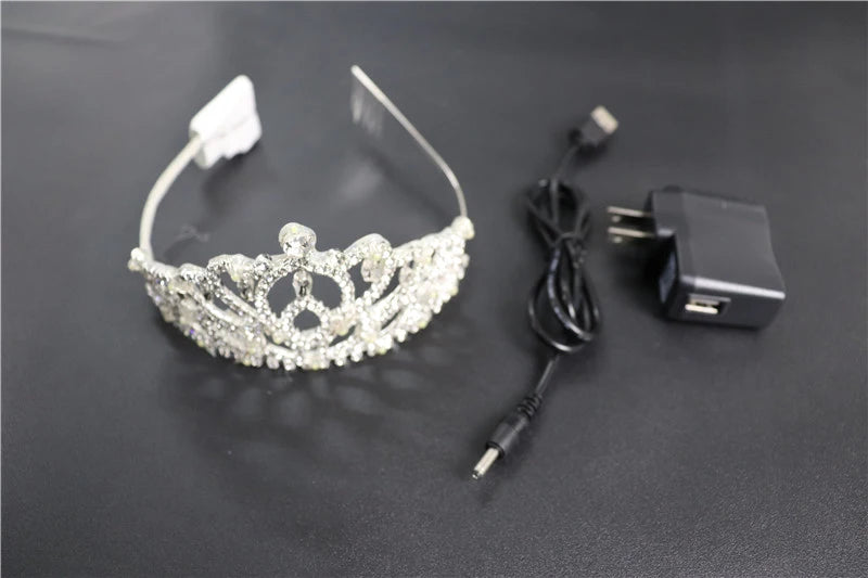 Silver rhinestone LED tiara with a flexible band, accompanied by a black USB charging cable and power adapter.