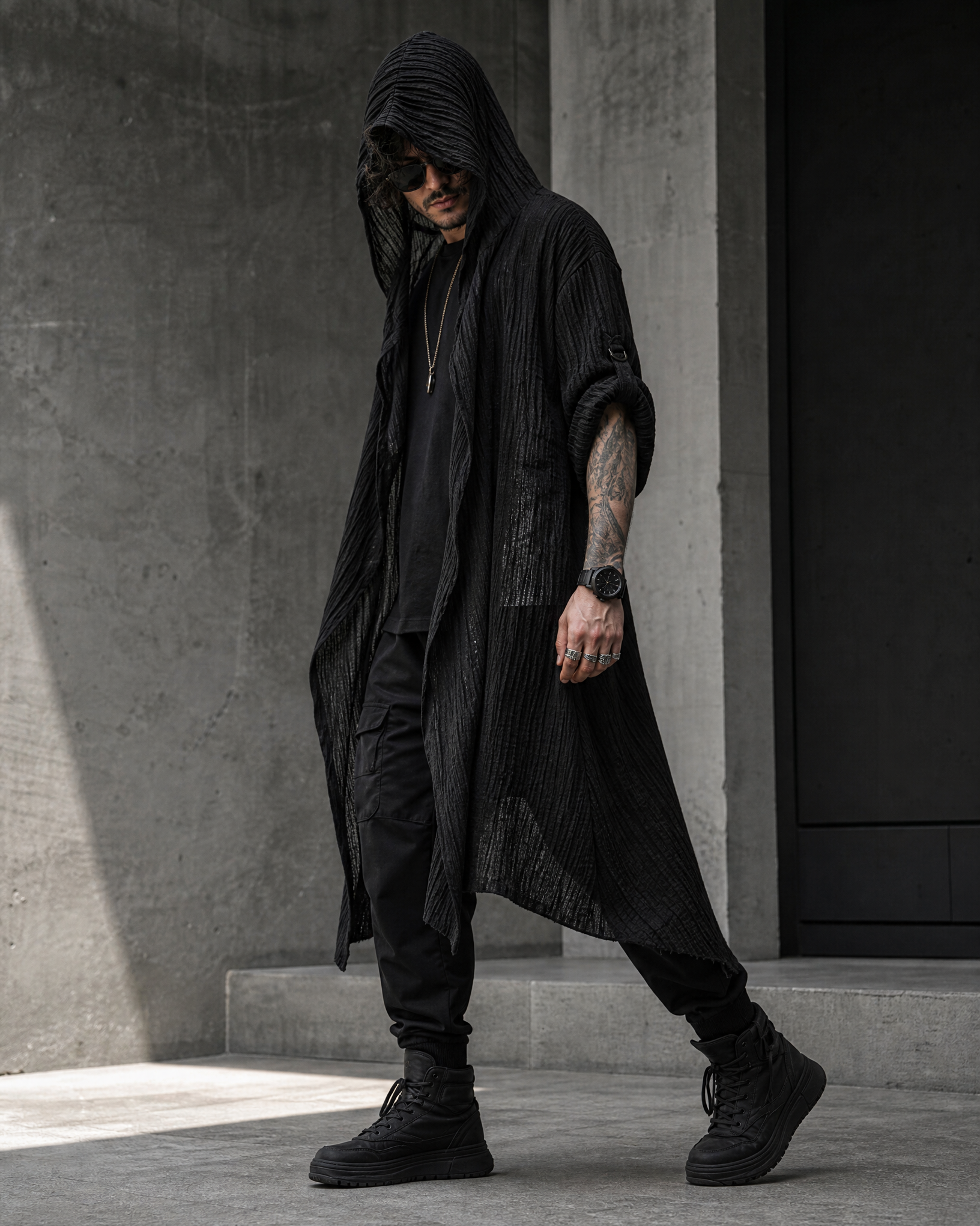 Man wearing a black, textured, long-sleeved hooded cardigan made of lightweight polyester in a modern, edgy style.