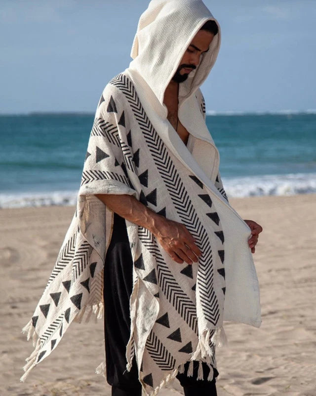 Men's Tulum Fringe Cardigan in cream polyester with black geometric patterns and a hood, worn on a beach.
