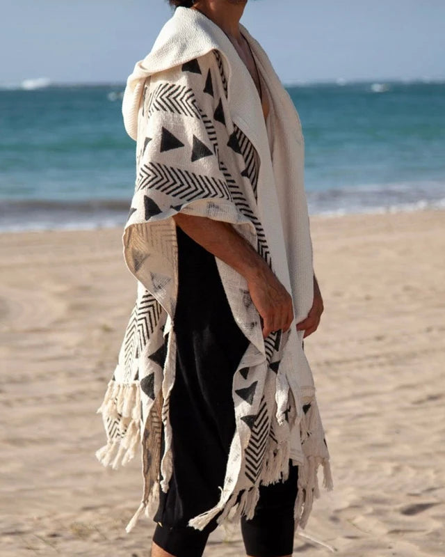 Men's Tulum Fringe Cardigan: cream polyester with black geometric print, hooded, open front, fringe hem, beach setting.