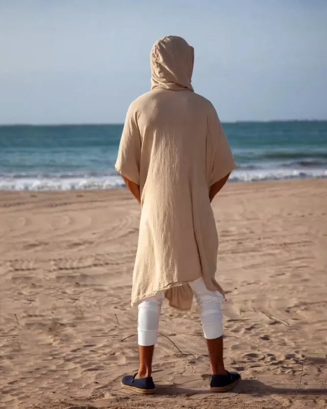 Men's sand polyester hooded cape with wide bat-wing sleeves, viewed from behind on a beach.