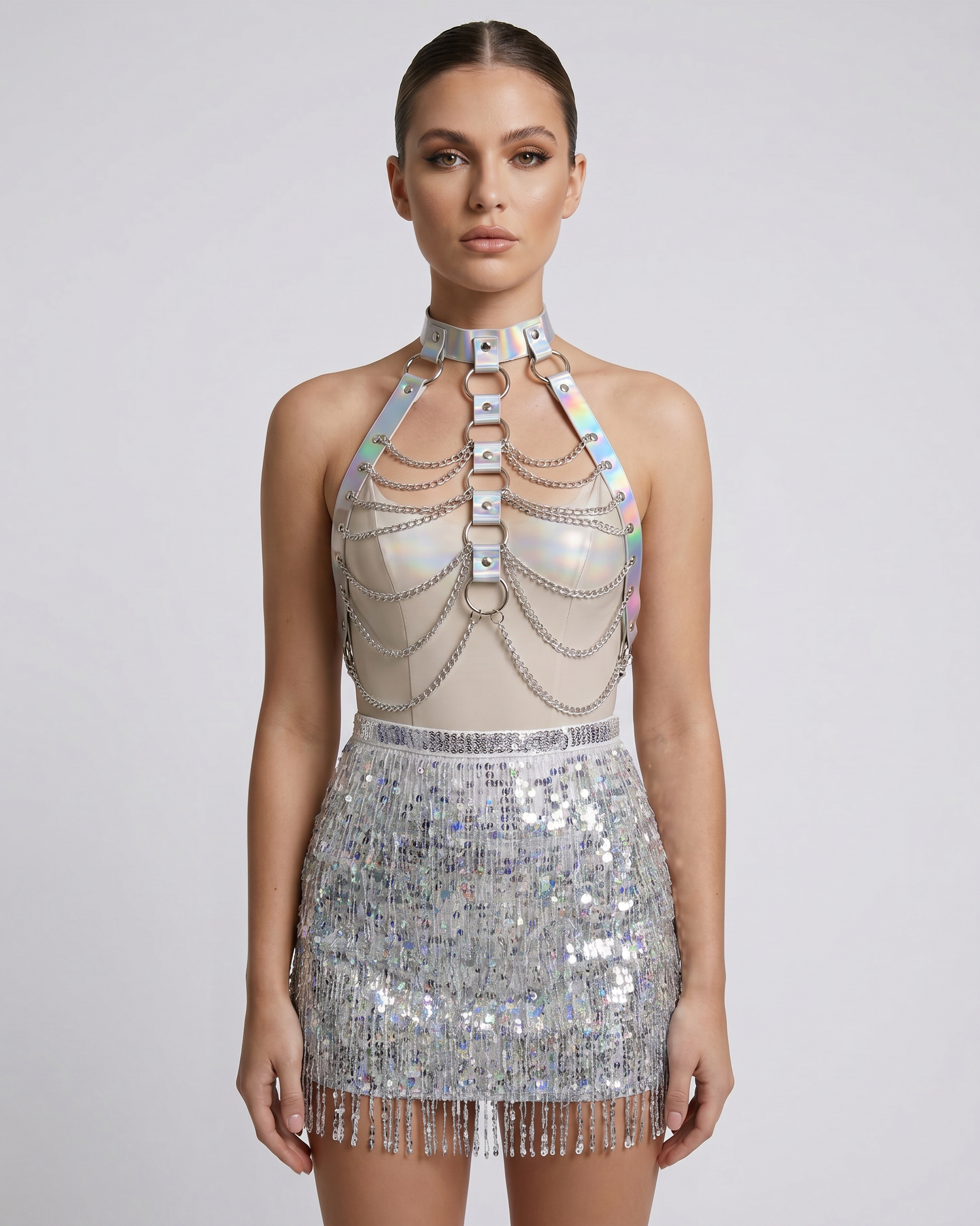Model wearing a silver holographic chest harness with metallic chains over a sequin fringe mini skirt.