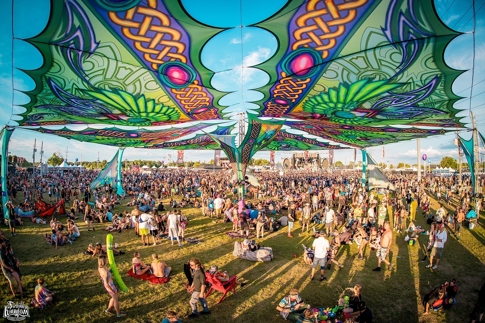 Vibrant festival crowd under colorful, patterned shade structures at an outdoor music event.