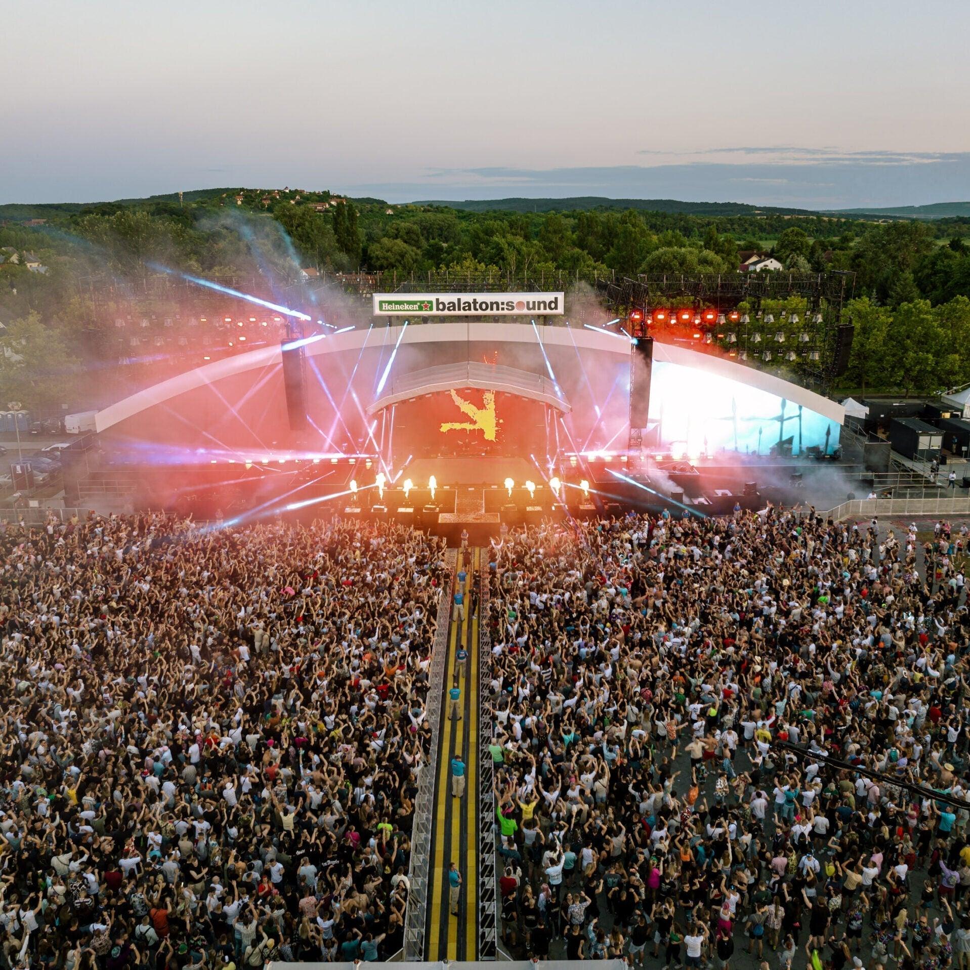 Aerial view of a massive crowd at Balaton Sound's brightly lit main stage with laser lights.