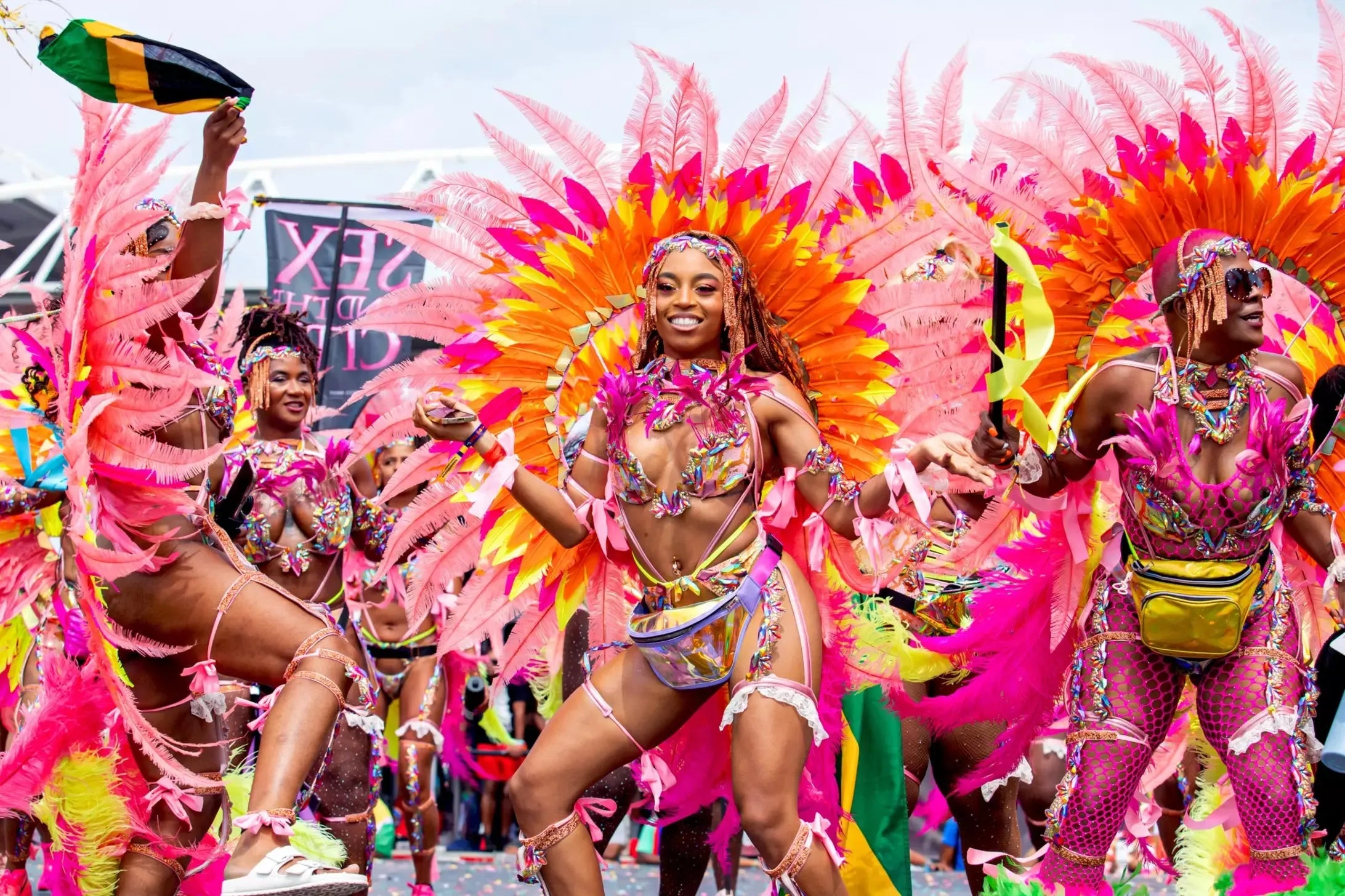 Carnival performers in vibrant pink and orange feathered costumes with intricate beadwork, celebrating Caribana.