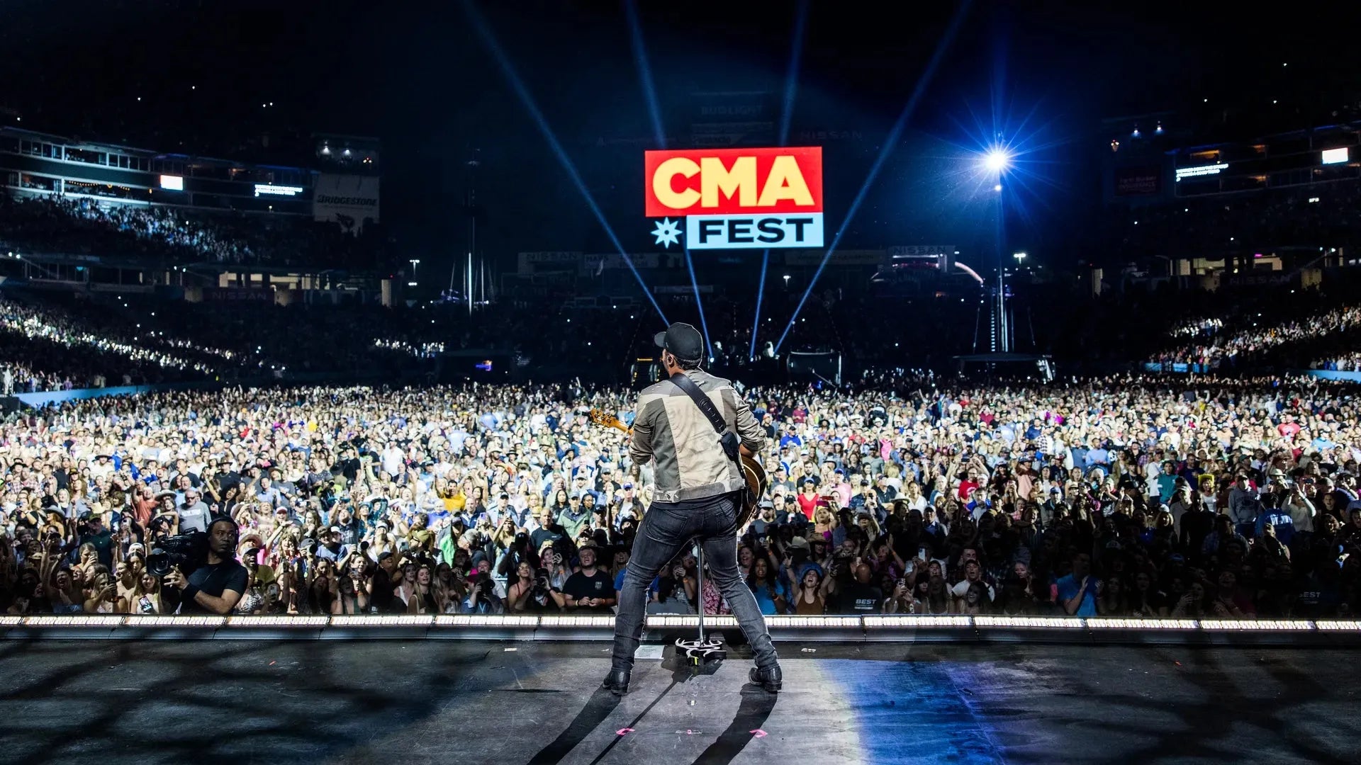 Artist on stage performing for a massive crowd at CMA Fest, with bright spotlights and the festival logo.