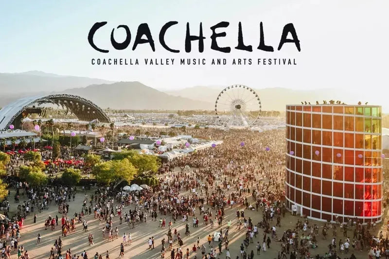 Aerial view of the crowded Coachella festival grounds with a Ferris wheel, stage, and colorful art installation.