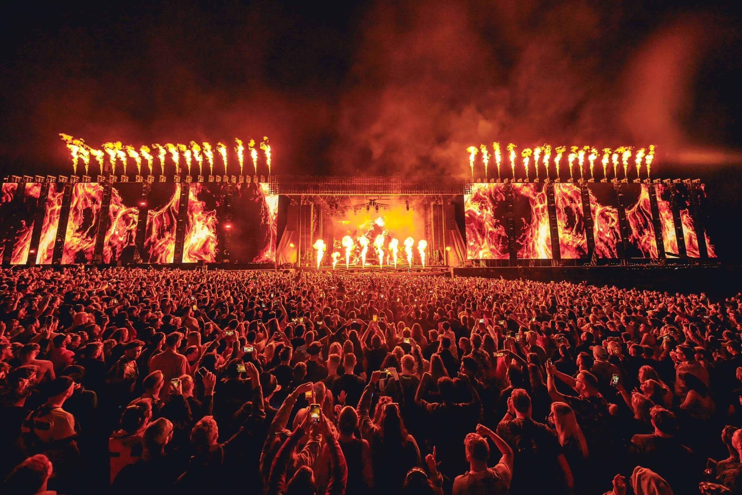 Massive crowd at Creamfields UK, illuminated by a fiery main stage with pyrotechnics and large screens.