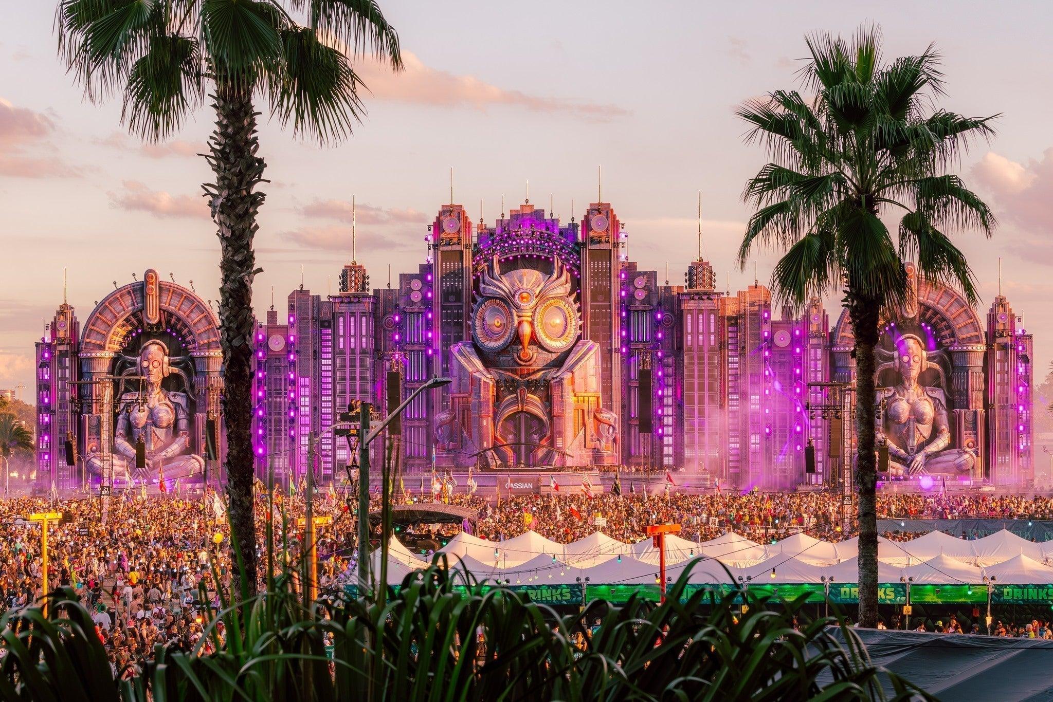EDC Orlando main stage with a giant owl, purple lights, palm trees, and a massive crowd.