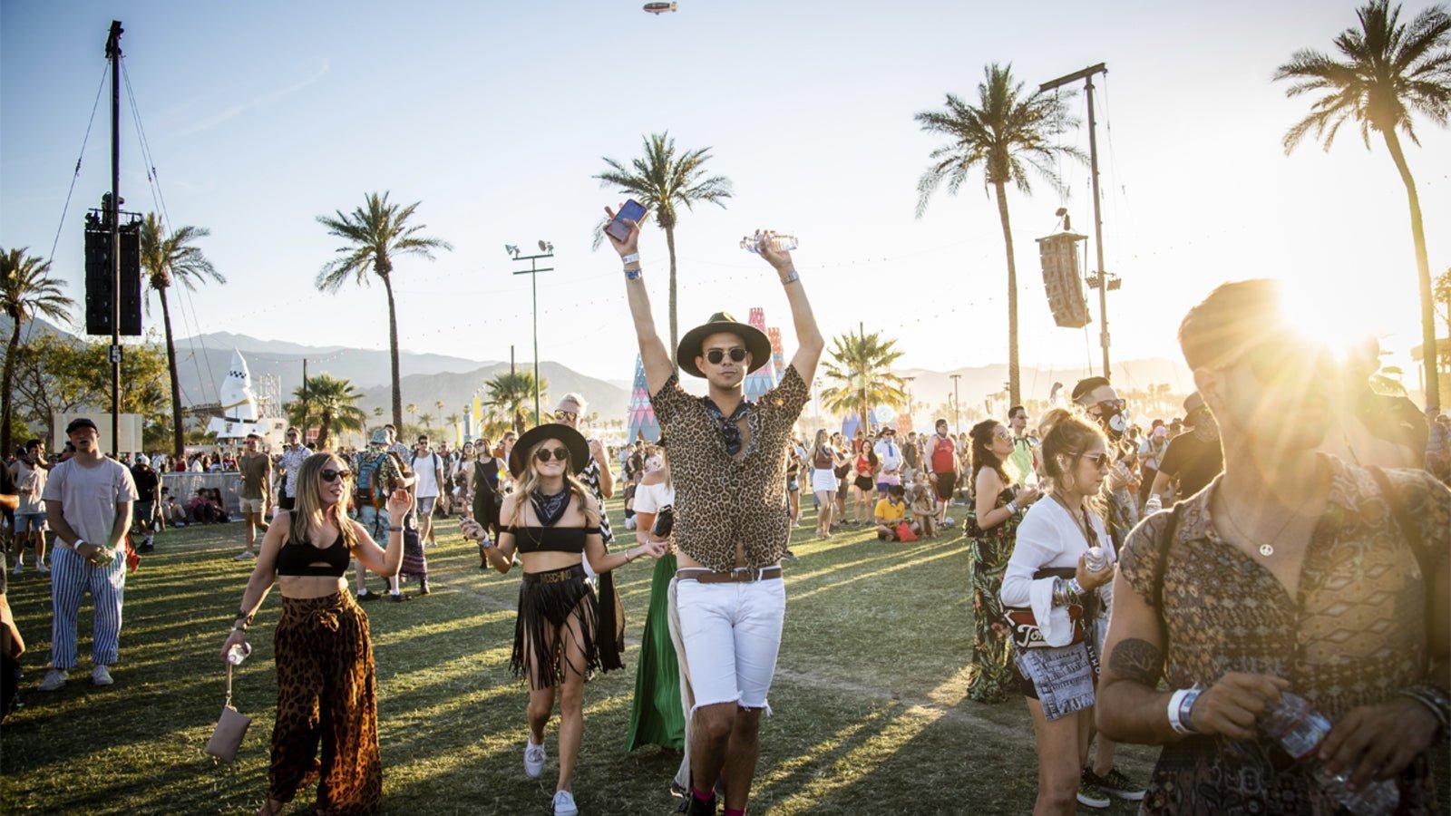 Joyful festival-goers in stylish outfits under palm trees at sunset, celebrating a music event.