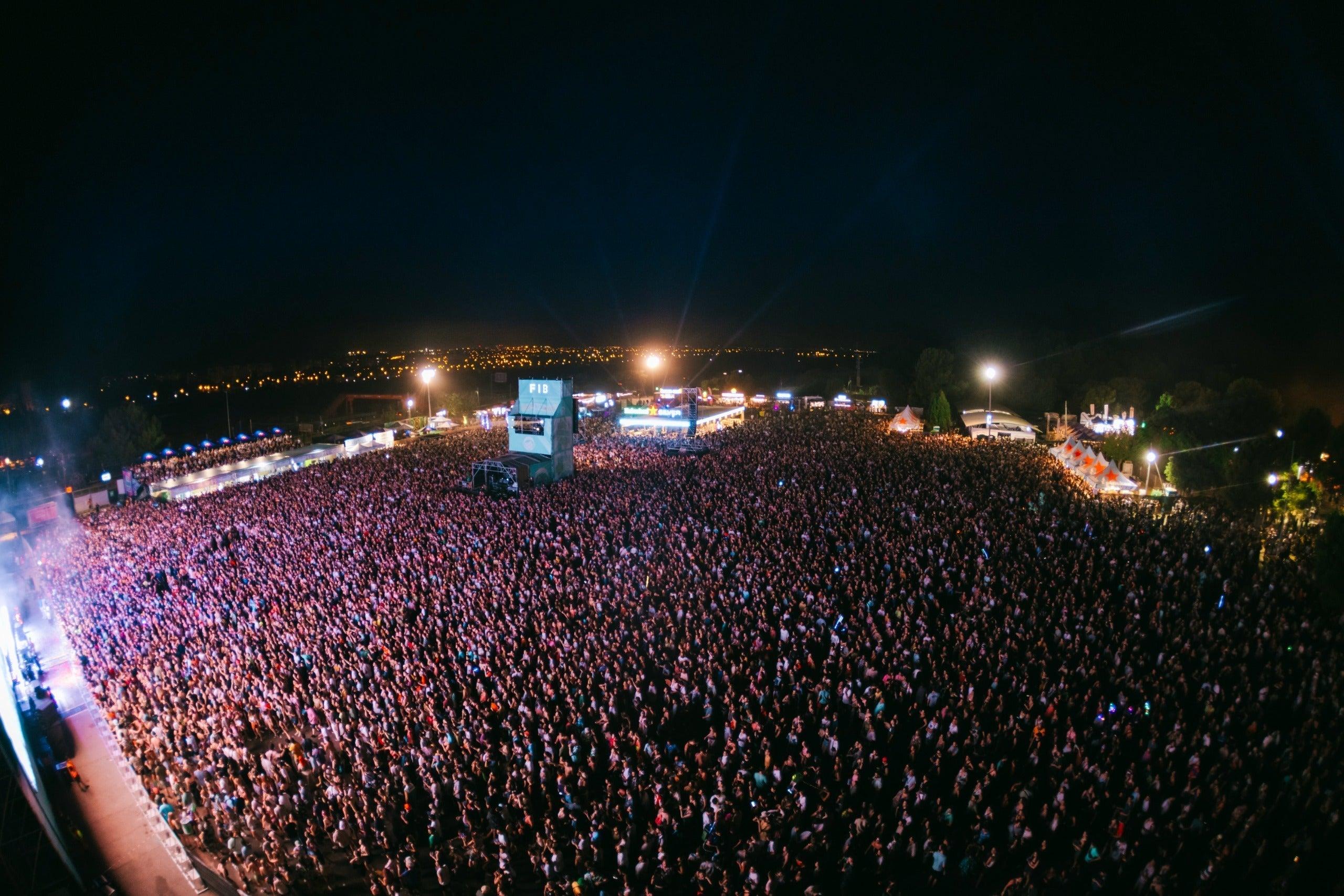 Vast crowd at FIB Benicassim festival at night, stage lights illuminating the audience under a dark sky.