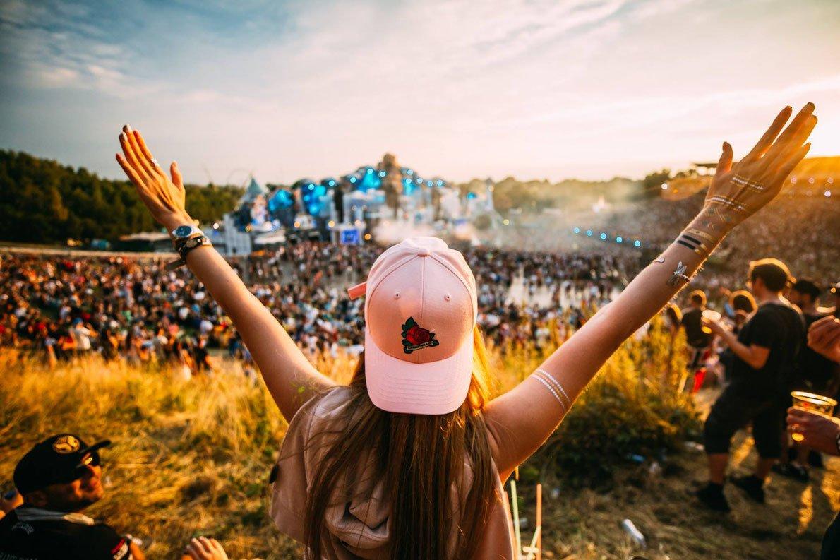 Person in a pink cap with arms raised, enjoying a vibrant outdoor music festival at sunset.