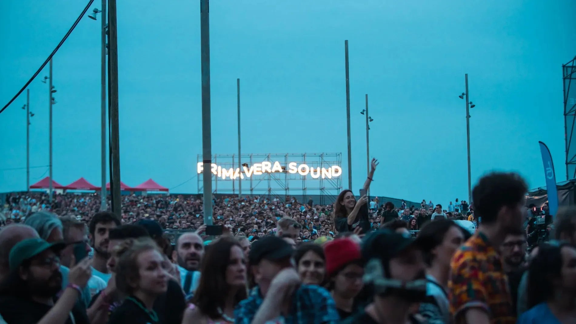 Crowd at Primavera Sound festival under a blue sky, with the illuminated "Primavera Sound" sign.