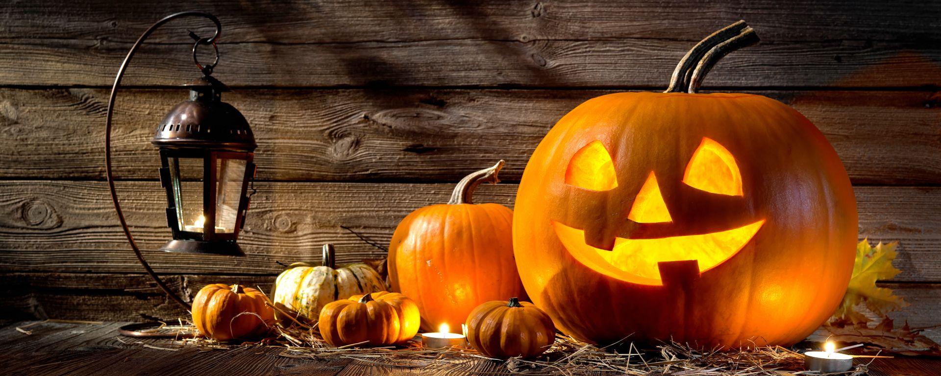 Glowing jack-o'-lantern, small pumpkins, and a lit lantern against rustic wood for Halloween.