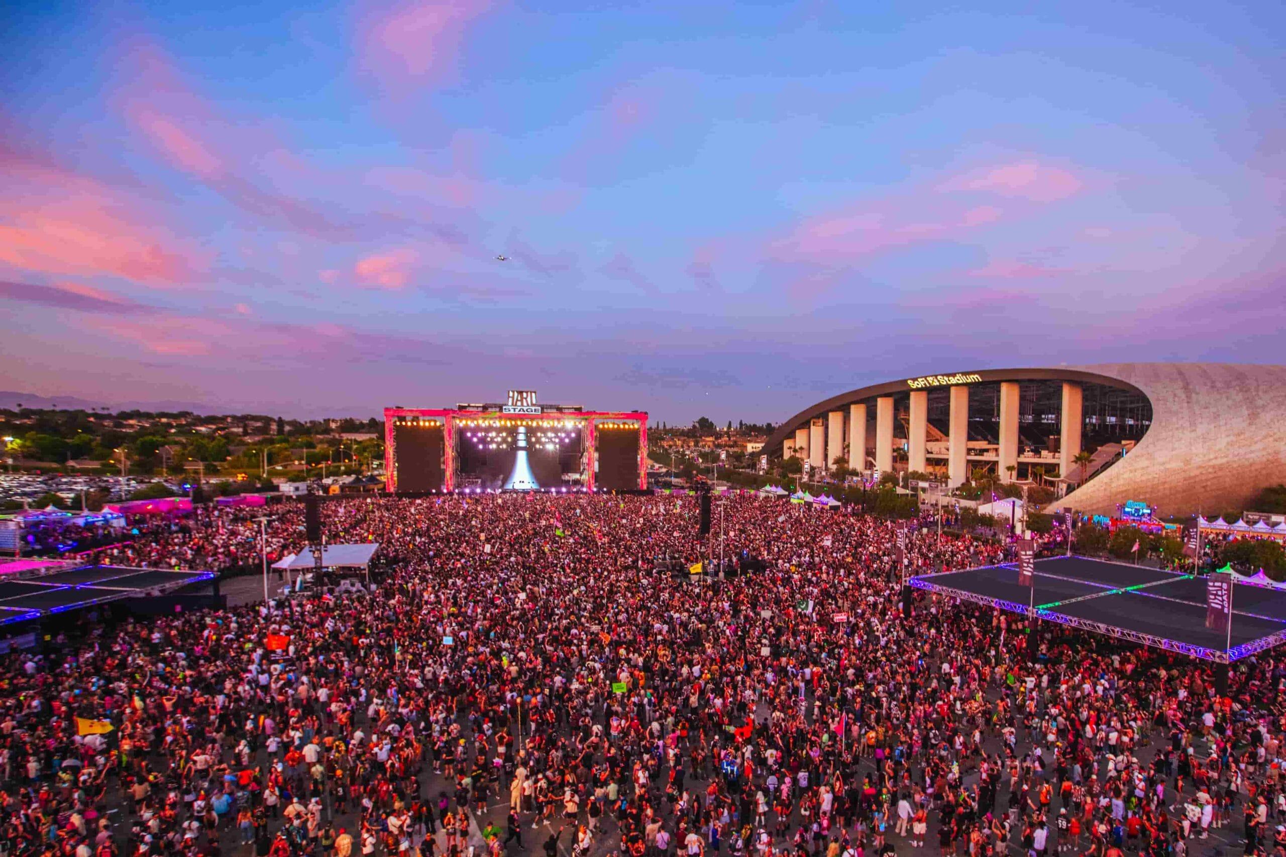 HARD Summer electronic music festival crowd at sunset, with a large stage and SoFi Stadium in the background.