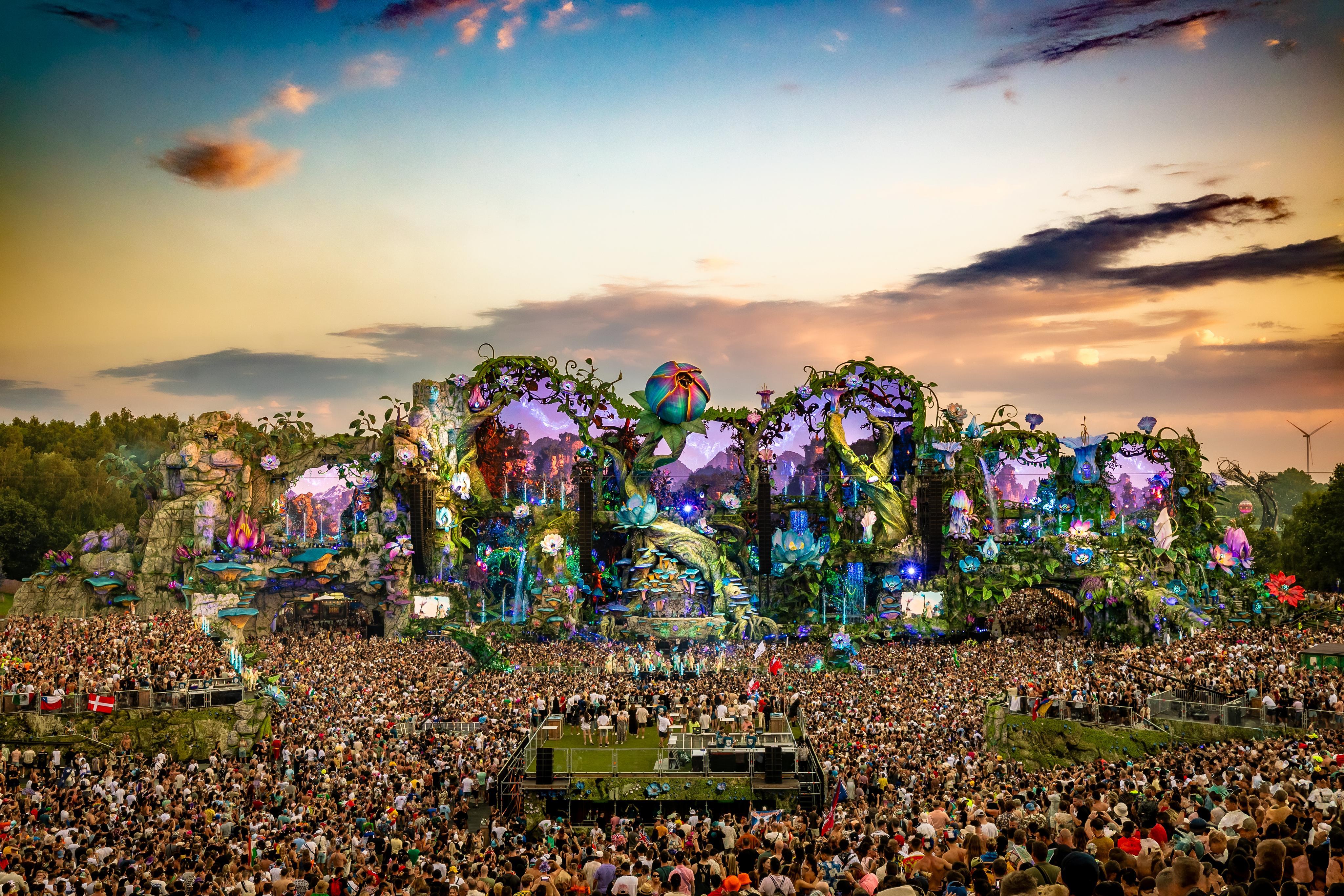 Tomorrowland main stage at sunset, with a massive crowd and intricate, fantastical decorations.