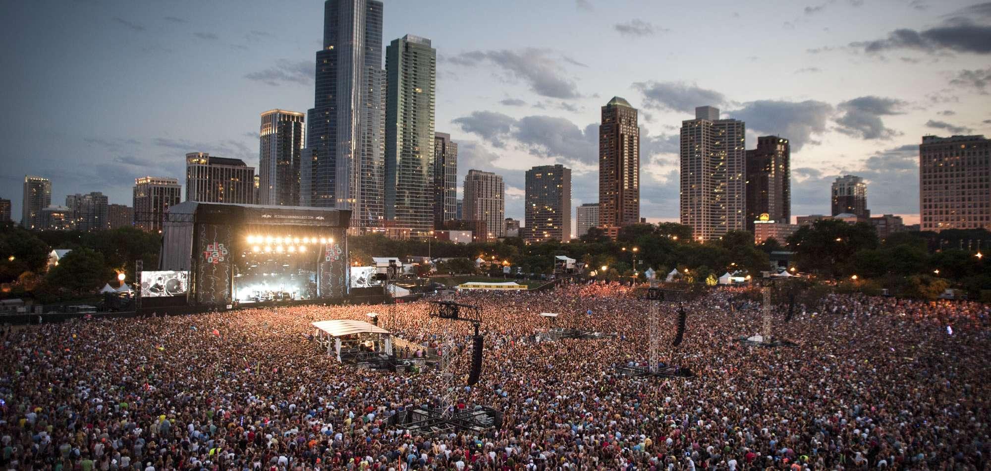 Vast crowd at a Lollapalooza concert in Grant Park, Chicago, with city skyline at dusk.
