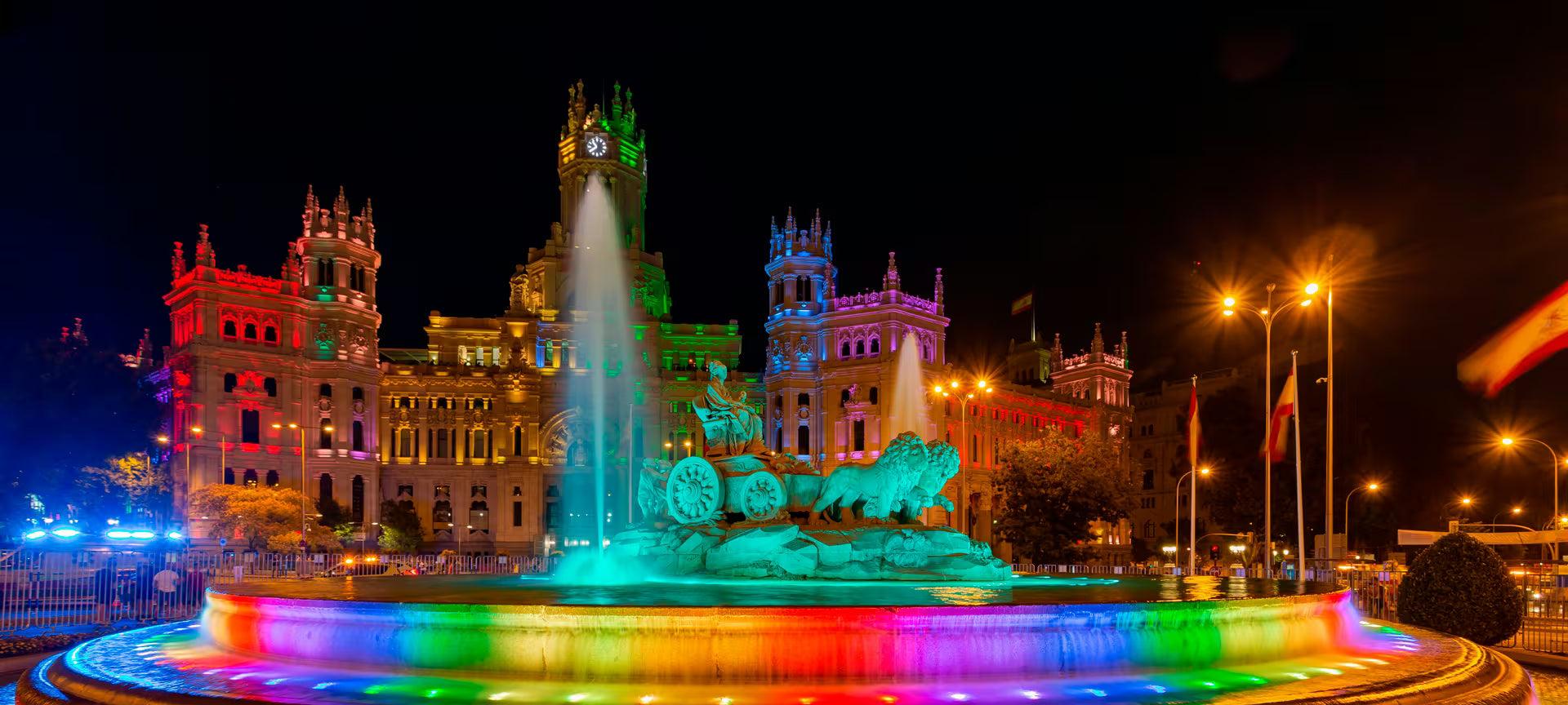 Cibeles Fountain and Palace lit with rainbow colors at night, celebrating Madrid Pride.
