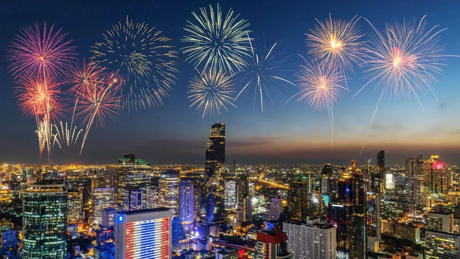 Vibrant New Year's Eve fireworks light up a modern city skyline at dusk, celebrating worldwide events.