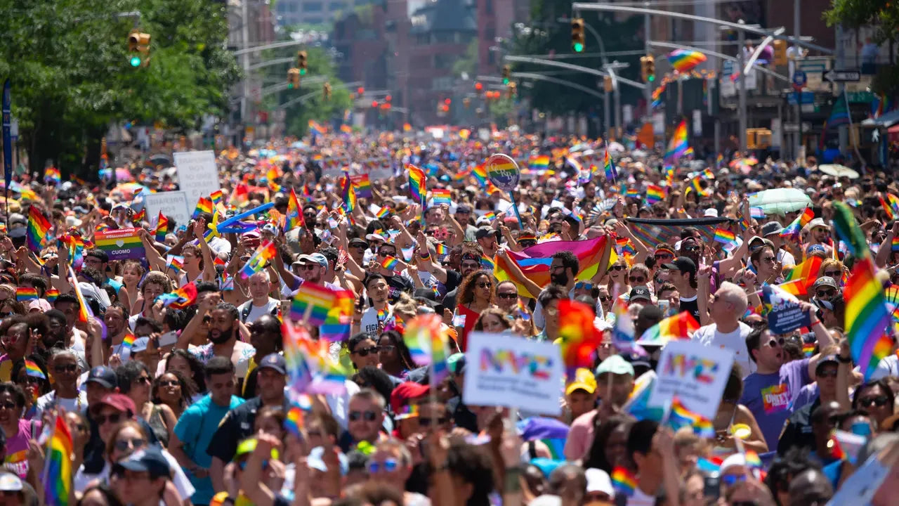 Vast crowd at NYC Pride March, waving rainbow flags under a sunny sky.
