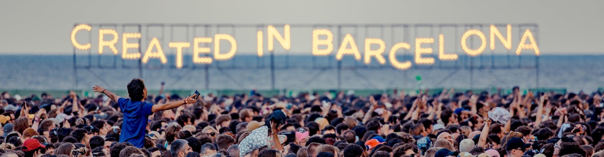 Festival crowd with arms raised under a large "CREATED IN BARCELONA" sign, celebrating music.