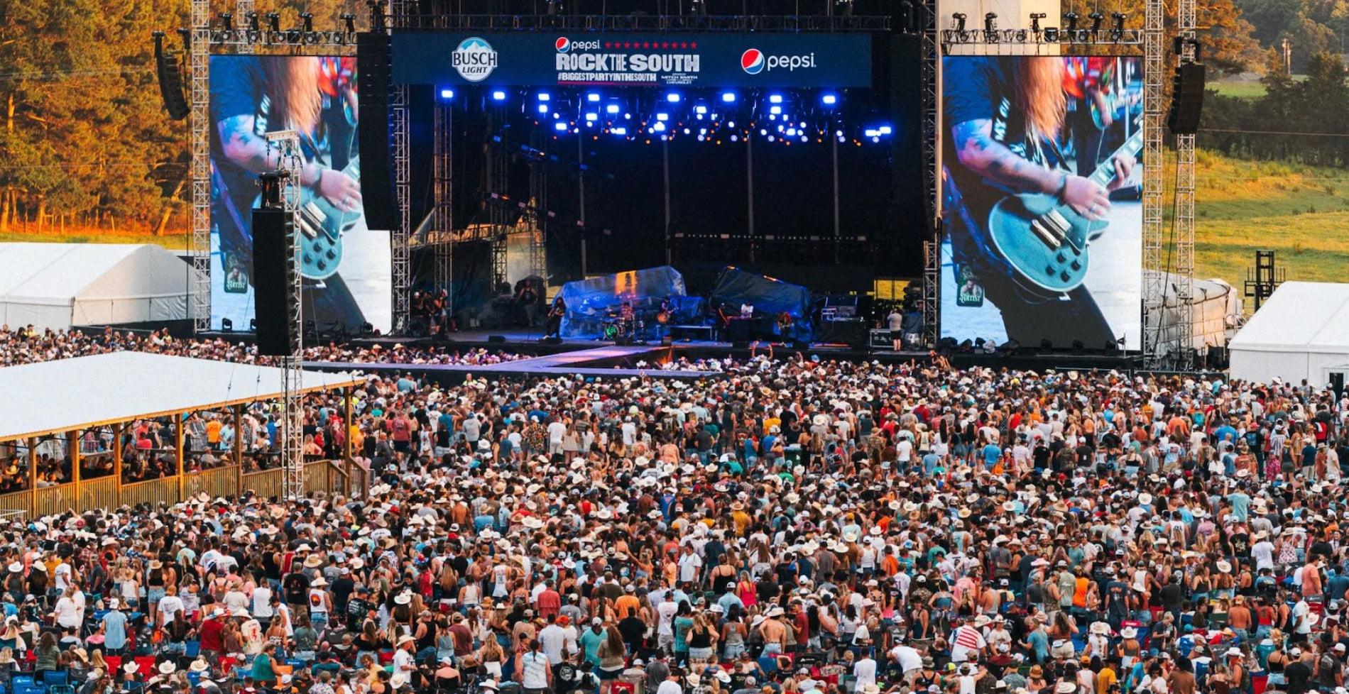 Crowd of country music fans at Rock the South festival, with a large stage and video screens.