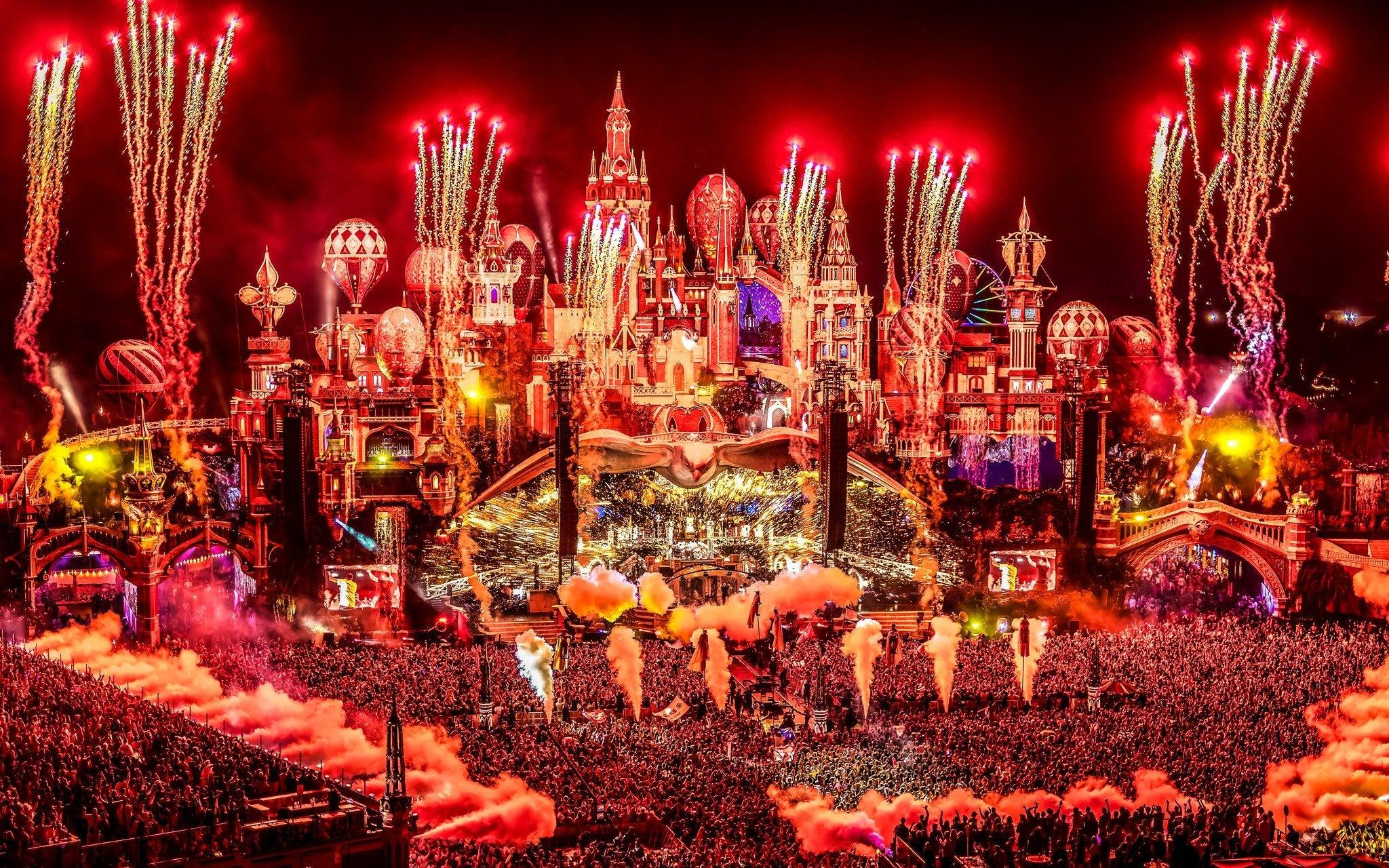 Tomorrowland mainstage at night, illuminated by red fireworks and lights over a massive crowd.