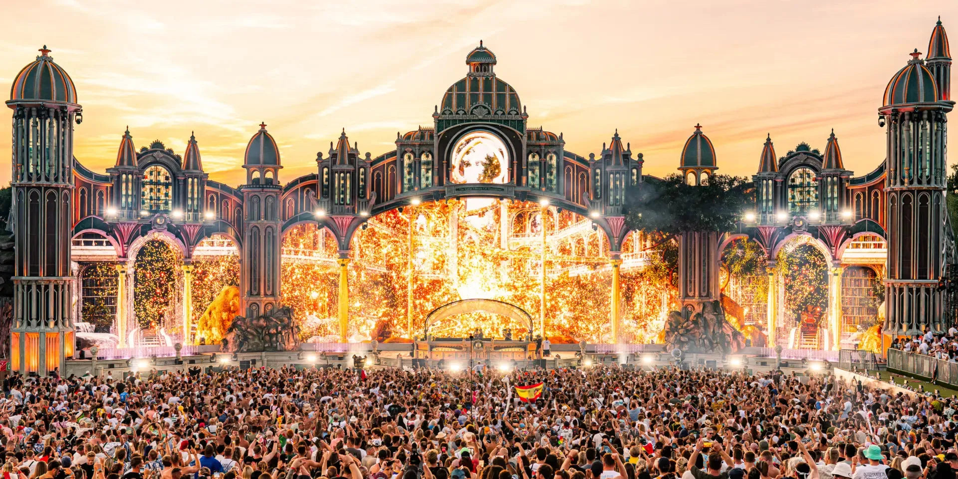 Tomorrowland's CONSCIENCIA main stage at sunset, with golden lights, fireworks, and a massive crowd.