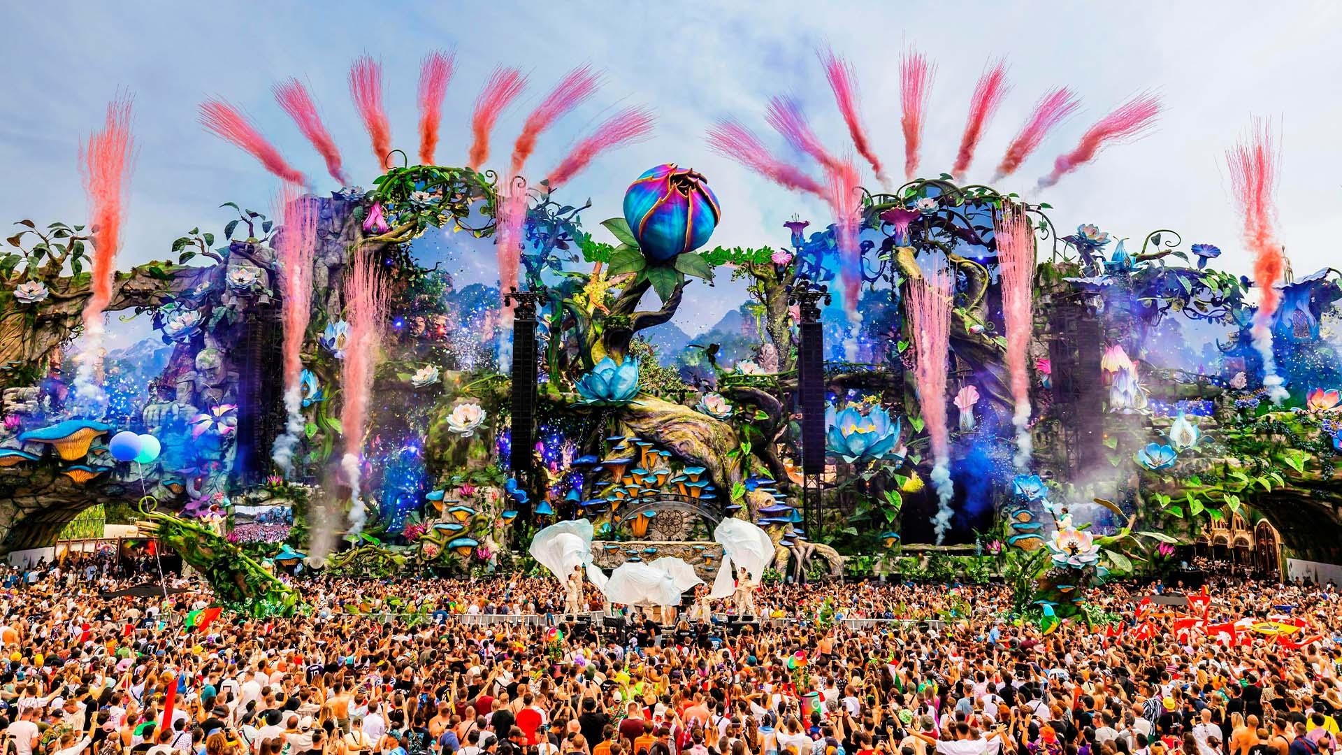 Tomorrowland main stage with vibrant floral decor, pink pyrotechnics, and a massive crowd.